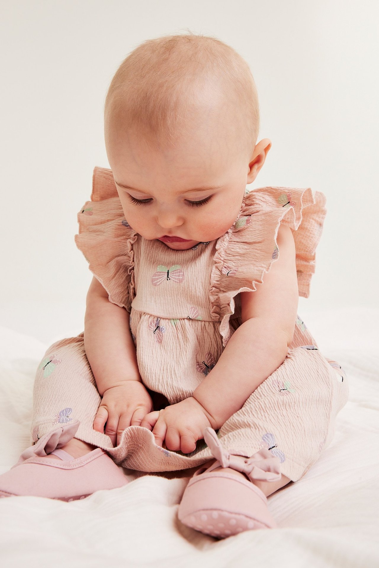 Widok z przodu: Niemowlę w różowej dżersejowej sukience w motyle, z falbanami i różowymi butami.