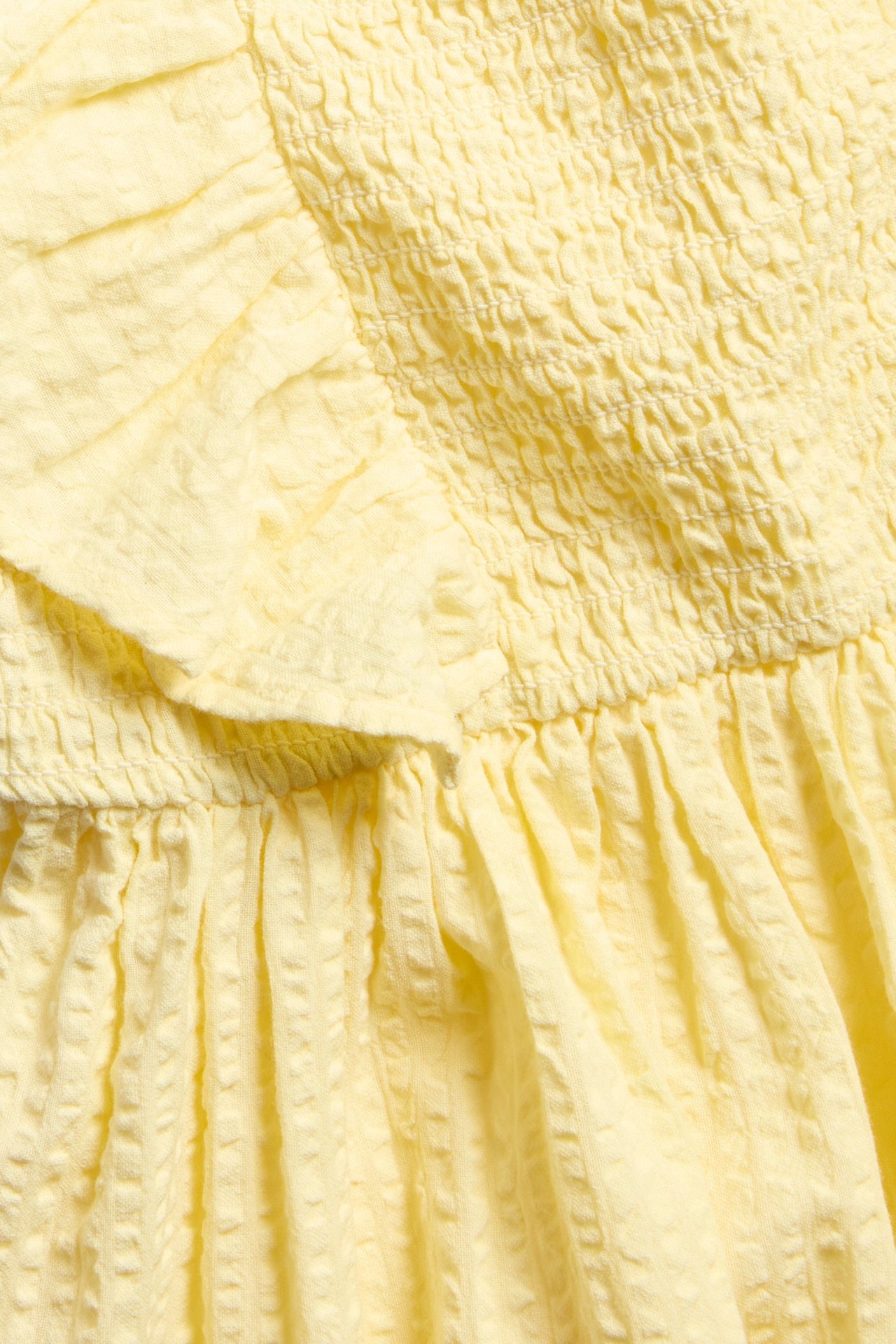 Nærbilde av en lysegul bomullskjole i bäckebölja med rynking og volang.