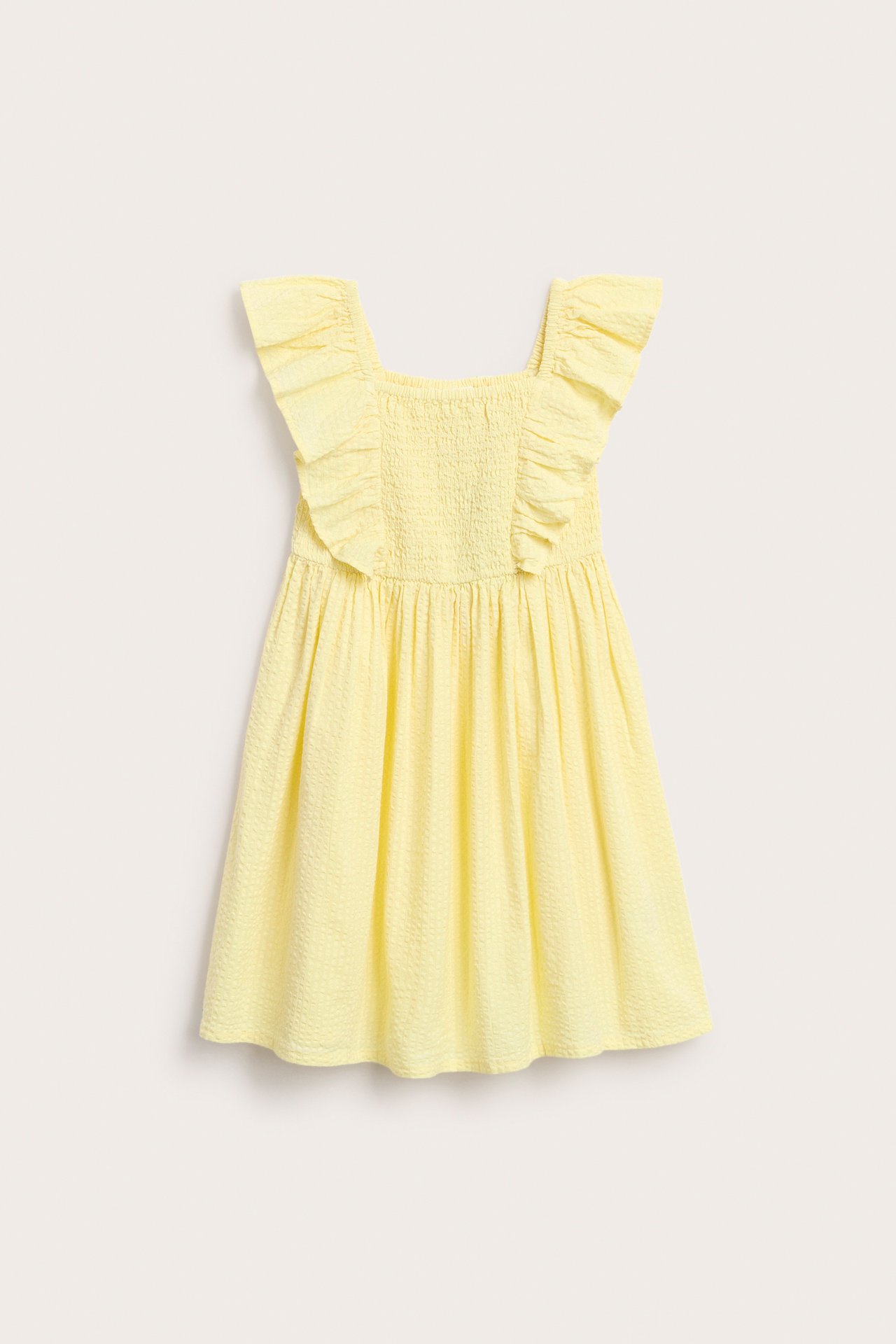 Edestä vaaleankeltainen lasten puuvillamekko, jossa röyhelöolkaimet ja smokattu yläosa.