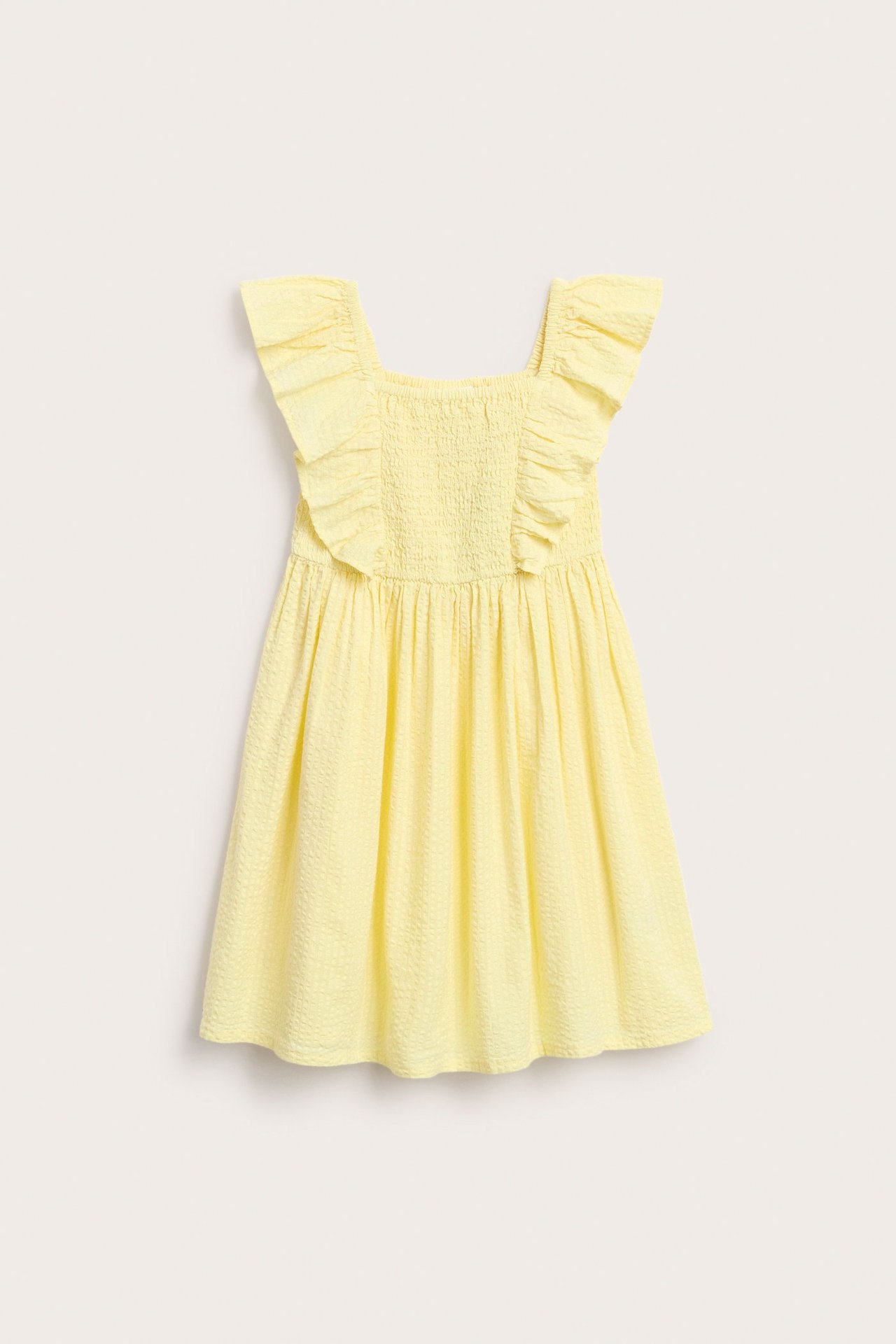 Forside av en lysegul barnekjole i bomull med volangskuldre og smocket overdel.