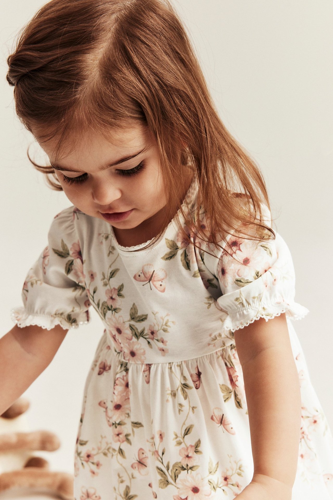 Zbliżenie: dziecko w złamanej bieli bawełnianej sukience z dżerseju, w kwiaty i motyle, z bufiastymi rękawami.