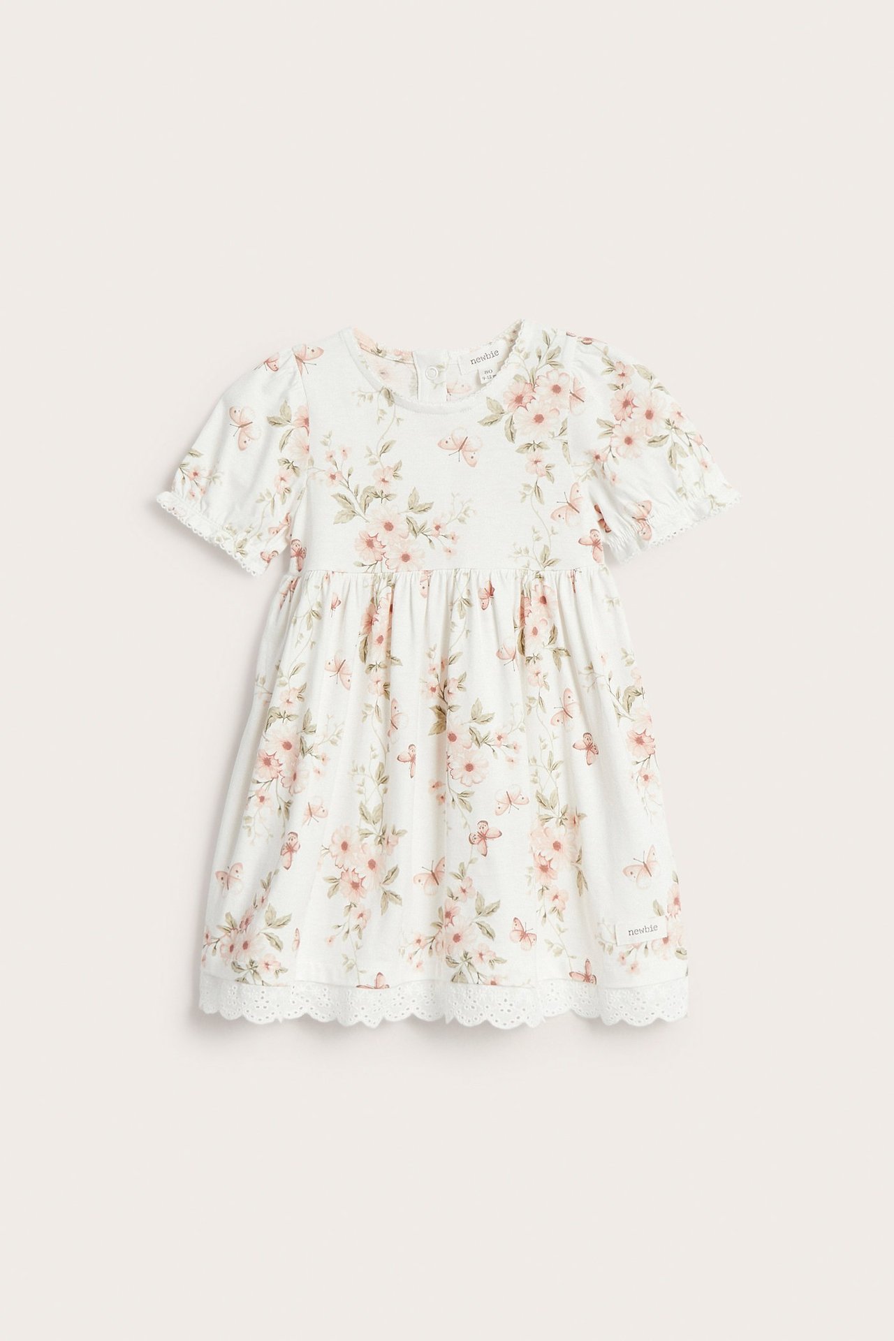 Frontside av en naturhvit barnejerseykjole med blomster- og sommerfugltrykk, puffermer og blondekant.