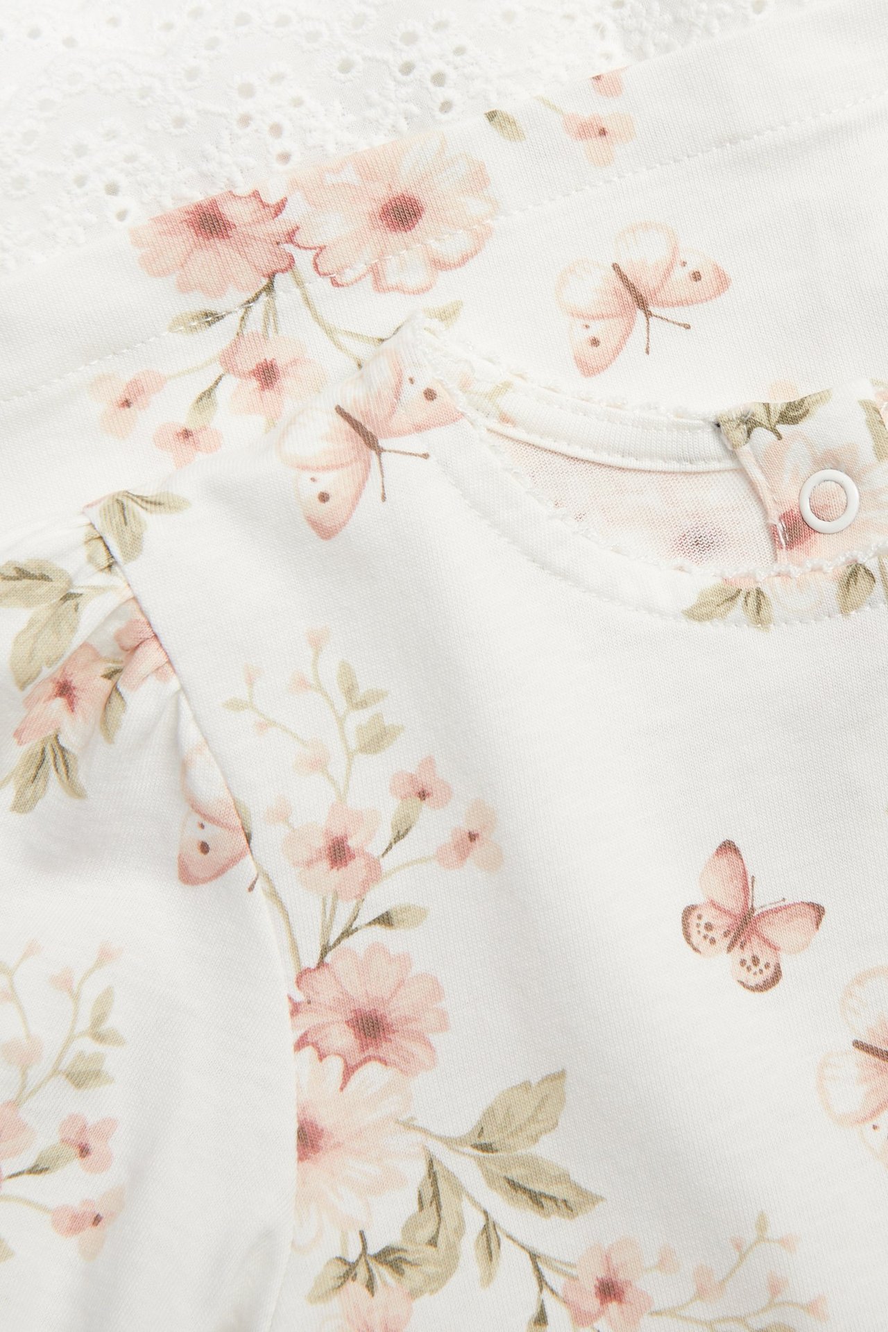 Zbliżenie: bawełniana sukienka ecru we wzór kwiatów i motyli, z okrągłym dekoltem, guzikiem z tyłu i koronką.