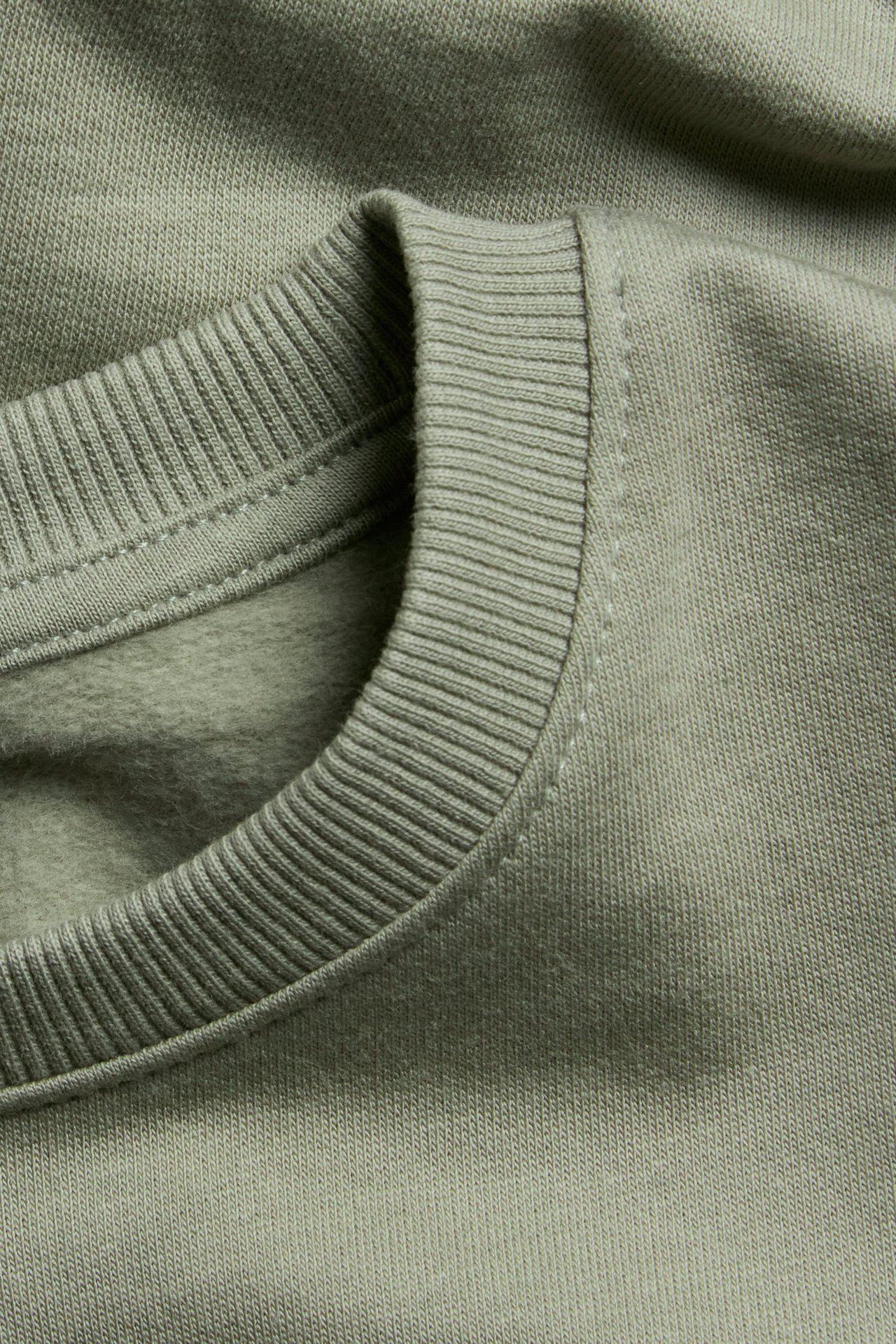 Zbliżenie na ciemnozieloną bawełnianą bluzę z prążkowanym dekoltem i szczotkowanym wnętrzem.
