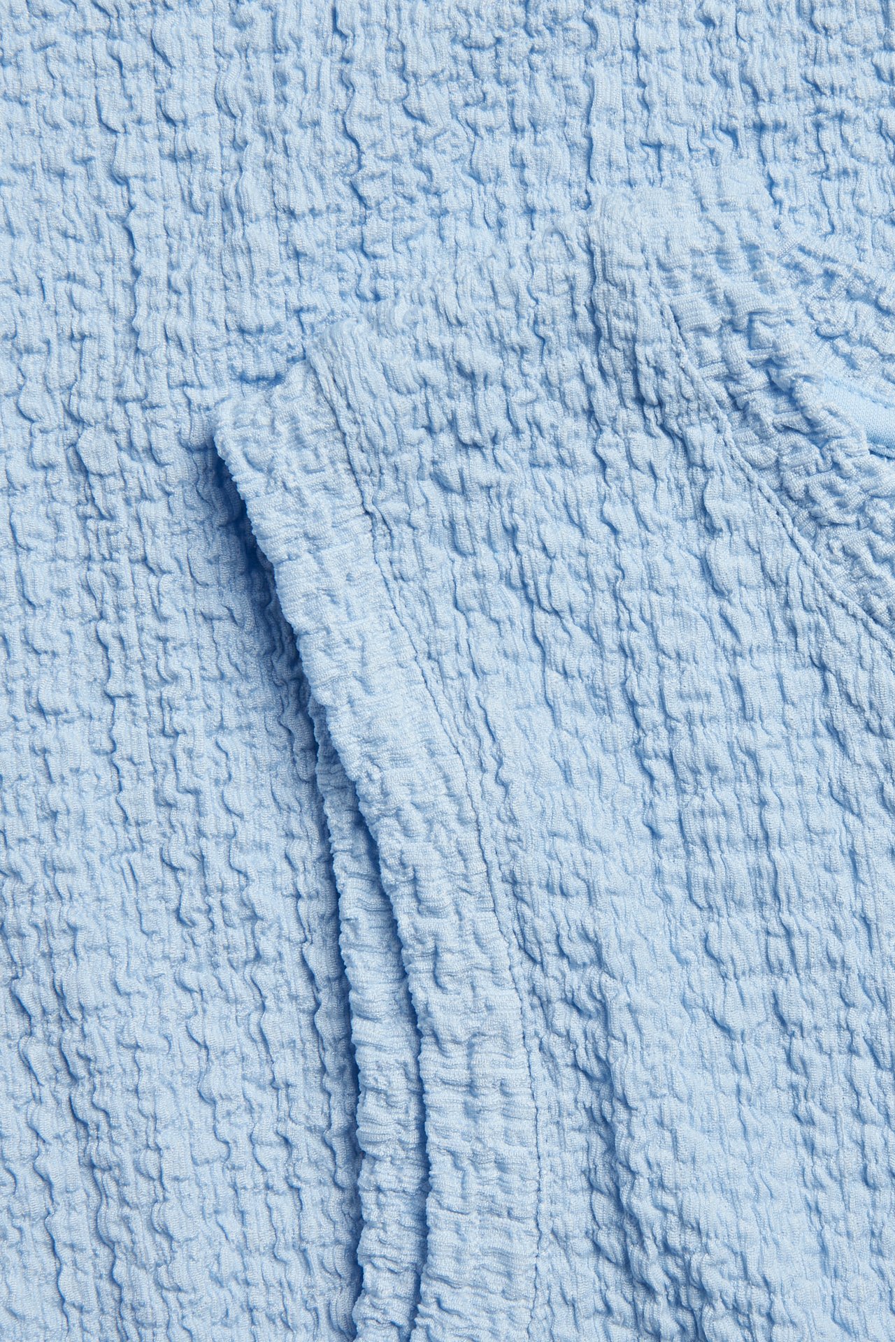 Lähikuva vaaleansinisestä strukturoidusta kankaasta, osa hihatonta midimekkoa.