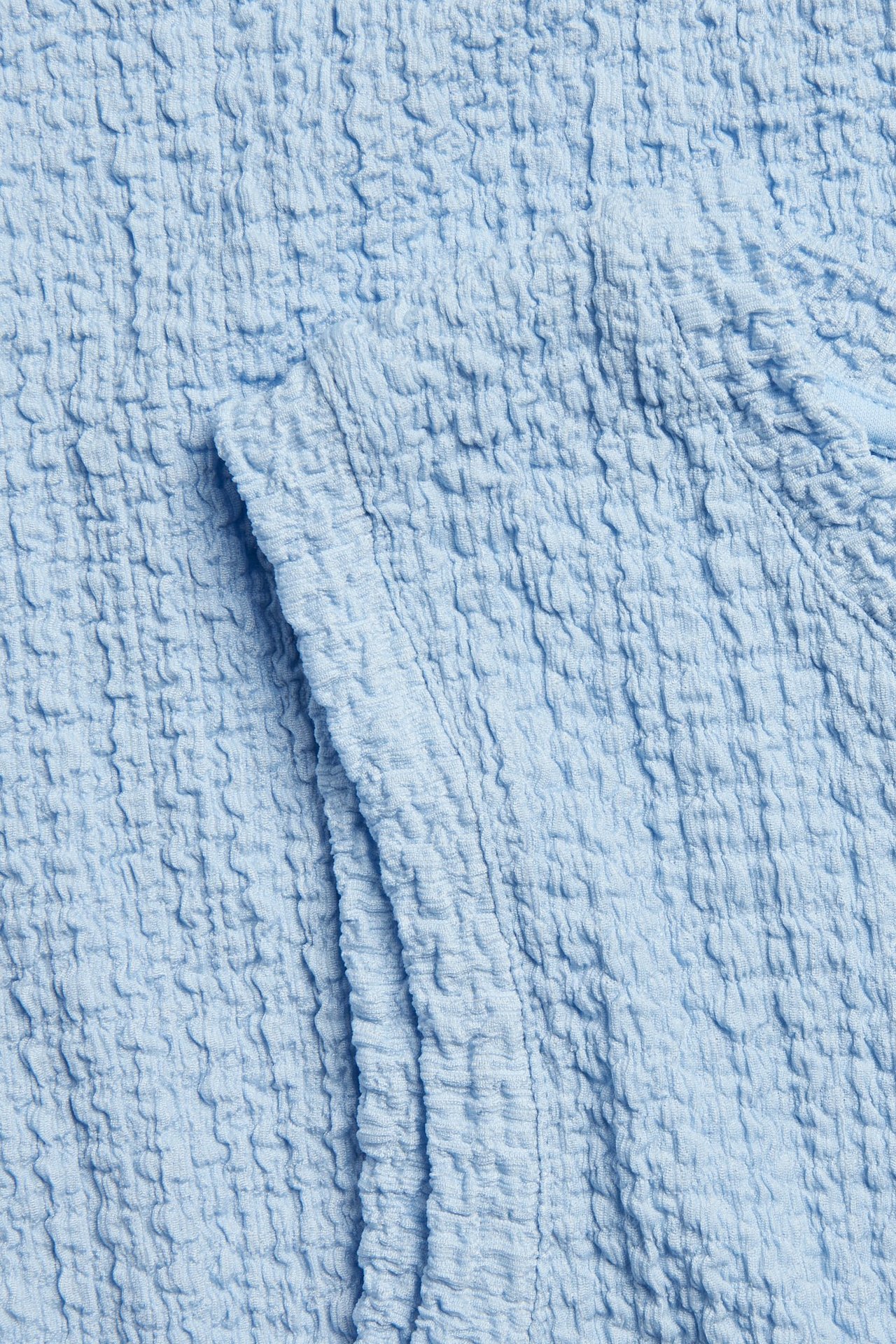 Närbild av ett ljusblått strukturerat tyg, del av en ärmlös midiklänning.