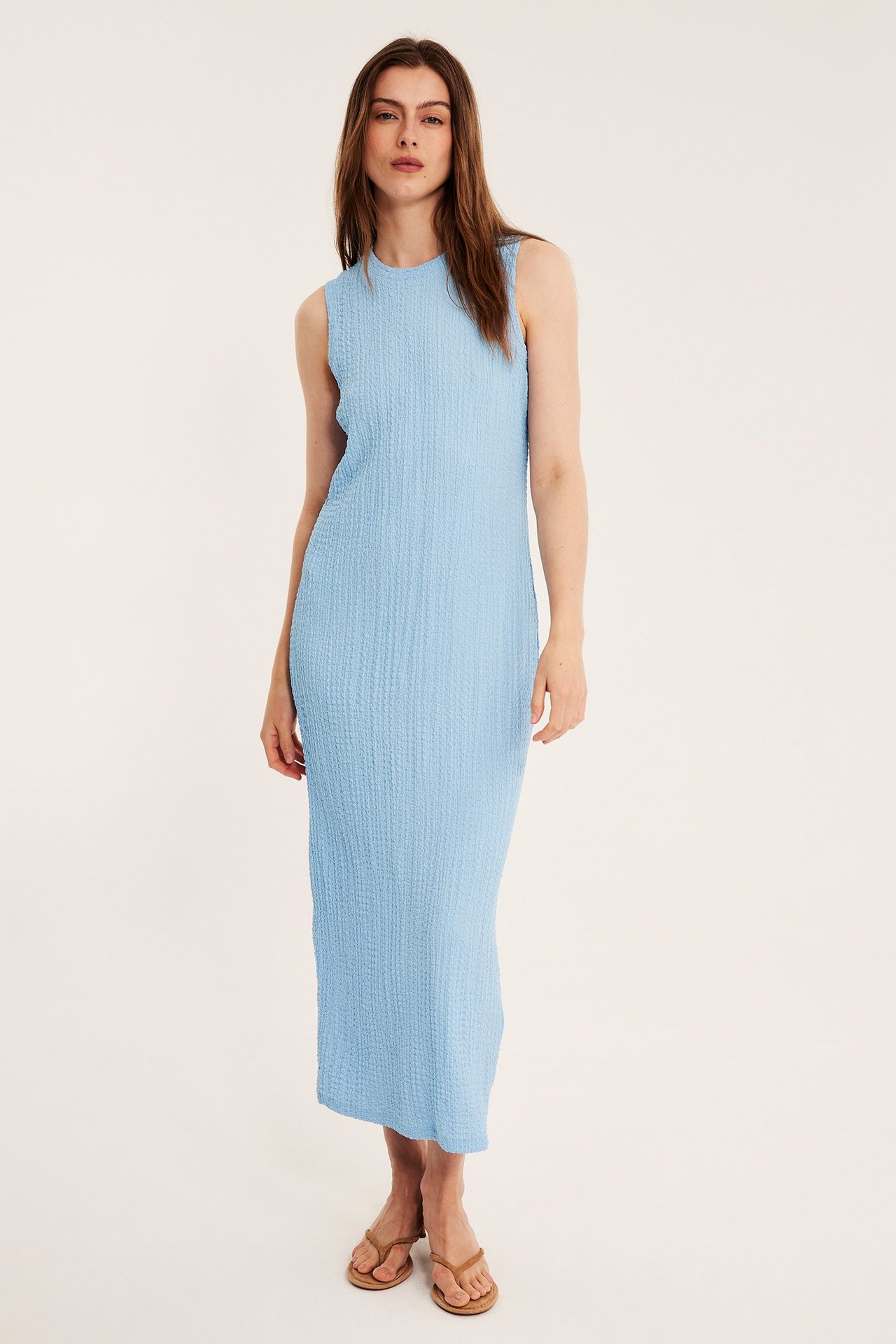 Edestä: Nainen yllään vaaleansininen kuvioitu hihaton midimekko, vaaleanruskeiden varvassandaalien kanssa.