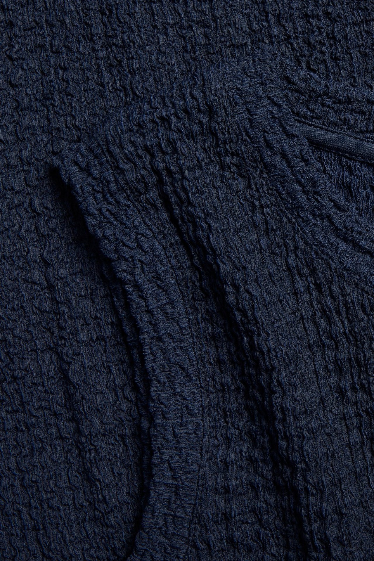 Närbild av mörkblått strukturerat tyg, del av en ärmlös midiklänning.