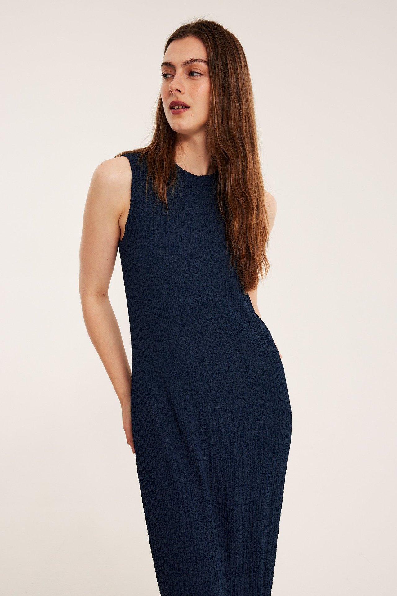 Edestäpäin, nainen yllään tummansininen hihaton midimekko, jossa on strukturoitu kangas.