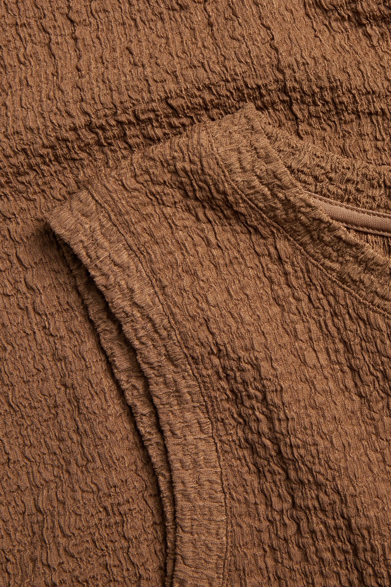 Närbild av en brun ärmlös midiklänning i strukturerat tyg.
