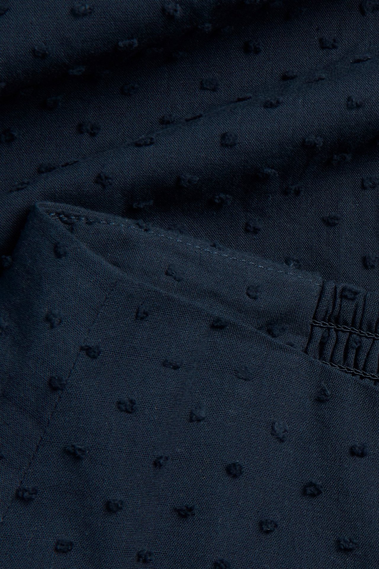 Nærbilde: mørkeblått bomulls-midiskjørt med prikkete mønster, synlige sømmer og smock-detaljer.