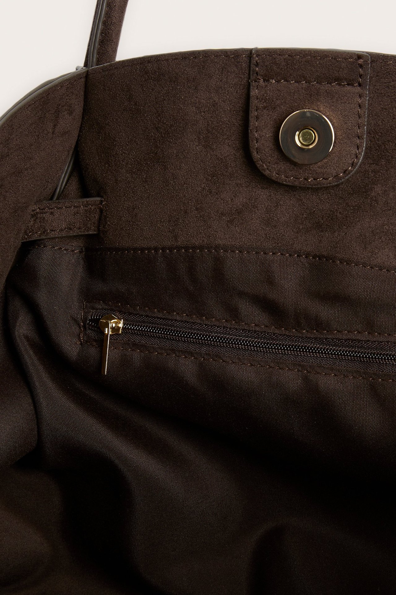 Närbild av en mörkbrun handväska i läderimitation, med magnetknapp och innerficka med dragkedja.