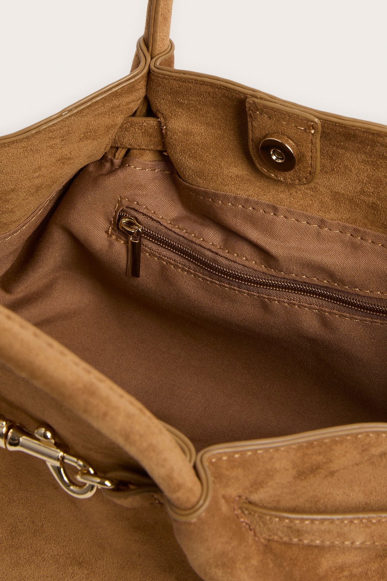 Närbild på öppen brun mockaimitationsväska med foder, innerficka med dragkedja och magnetknapp.