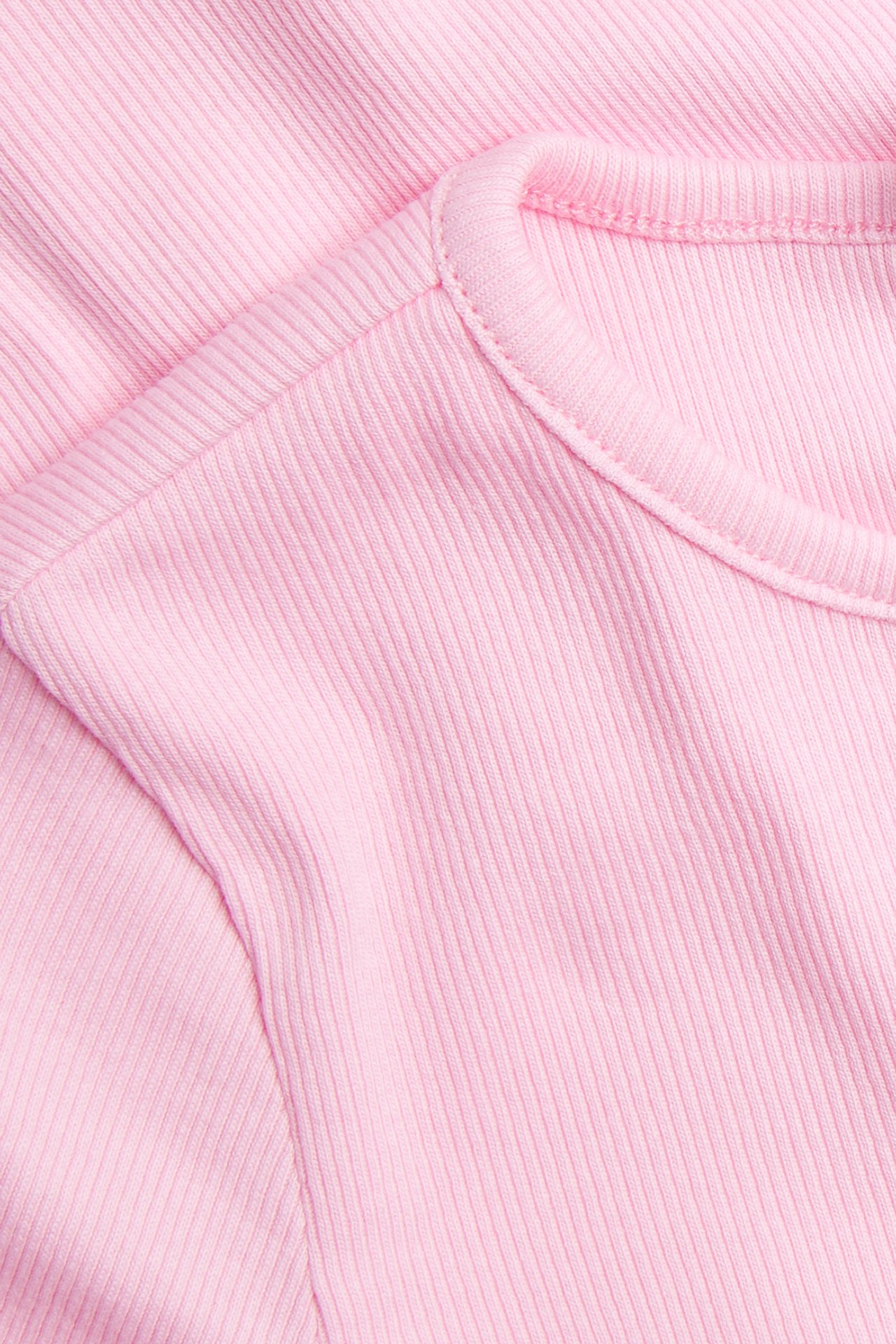 Nærbilde av en rosa ribbestrikket kortermet topp, som viser den runde halslinningen og det teksturerte økologiske bomullsstoffet.