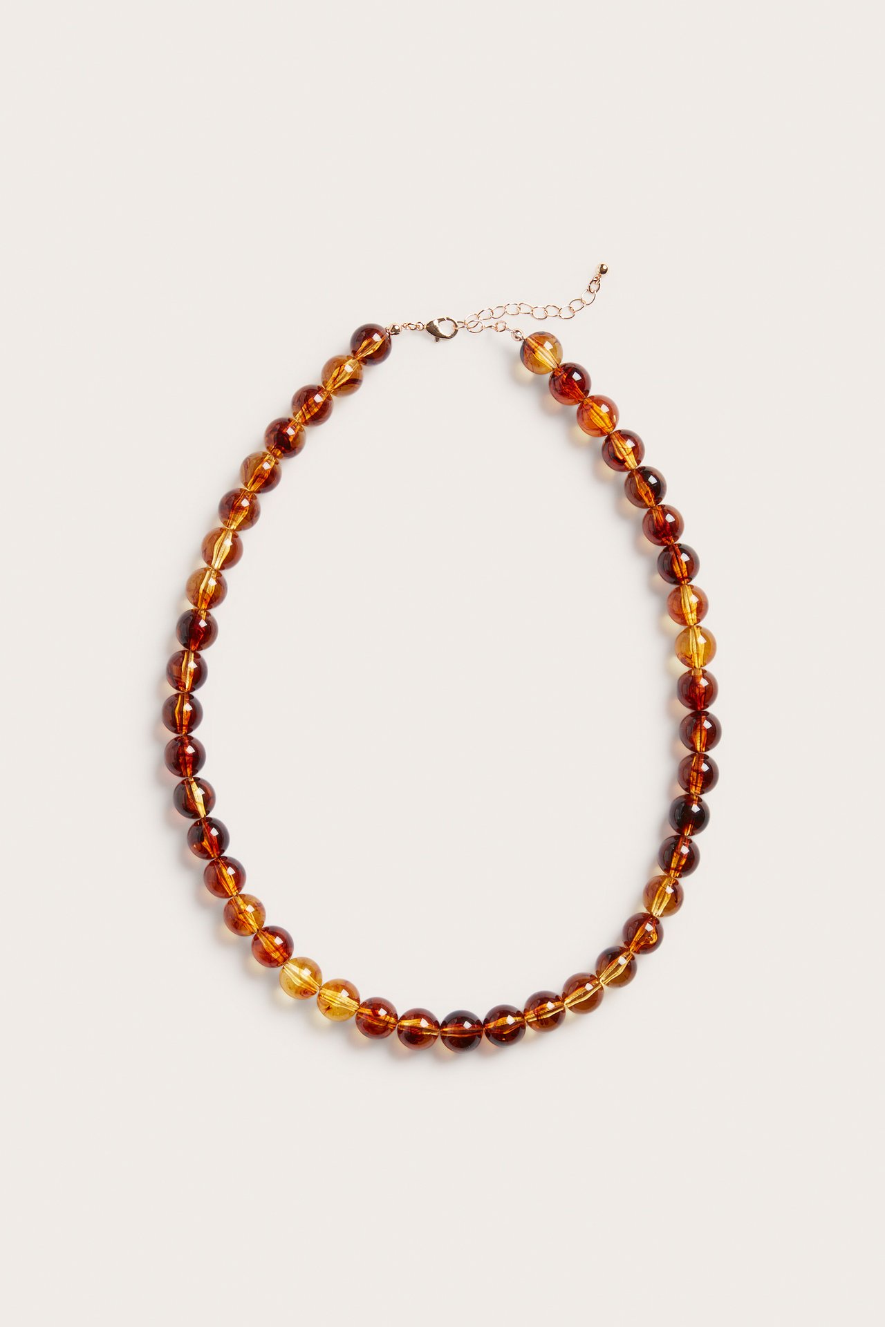 Närbild av ett bärnstensfärgat pärlhalsband med plastpärlor i olika bruna nyanser och metallås.