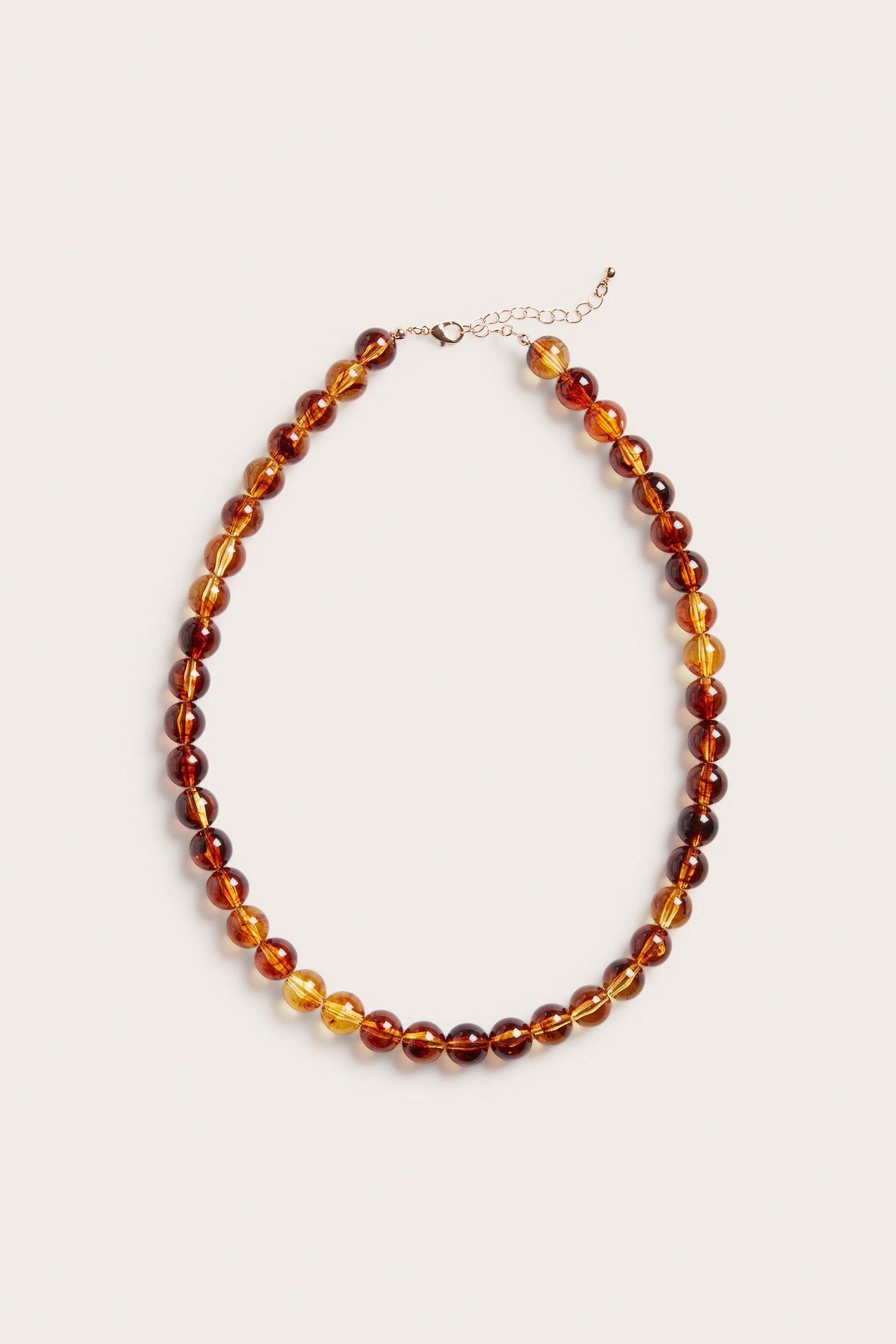 Nærbilde av et ravfarget perlekjede med plastperler i ulike bruntoner og metallås.