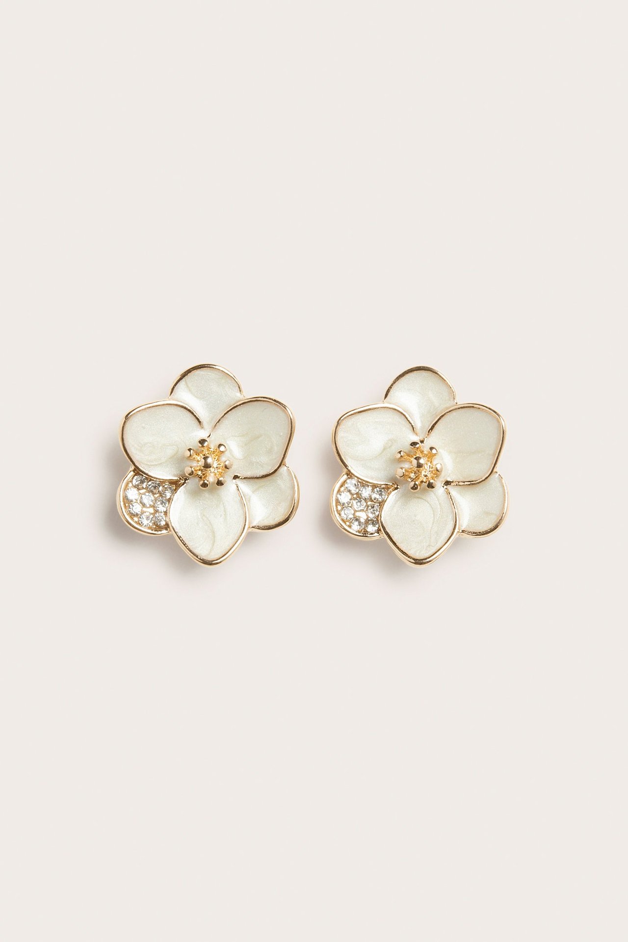 Lähikuva parista luonnonvalkoisesta kukanmuotoisesta korvakorusta kultaisilla reunoilla ja strassiyksityiskohdilla.