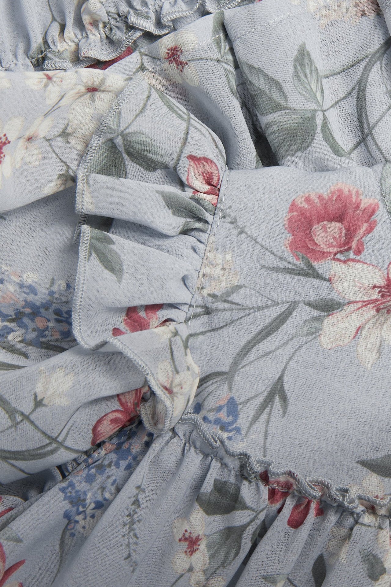 Zbliżenie na jasnoniebieską szyfonową sukienkę z kwiatowym wzorem i marszczonymi falbanami.