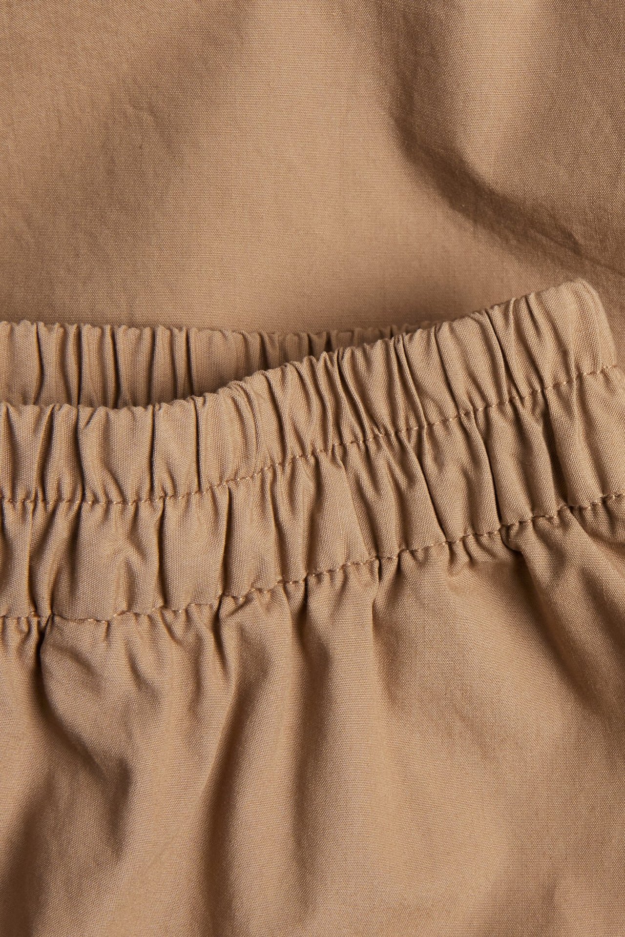 Närbild av en beige bomullspoplinkjol med elastisk, rynkad midja.