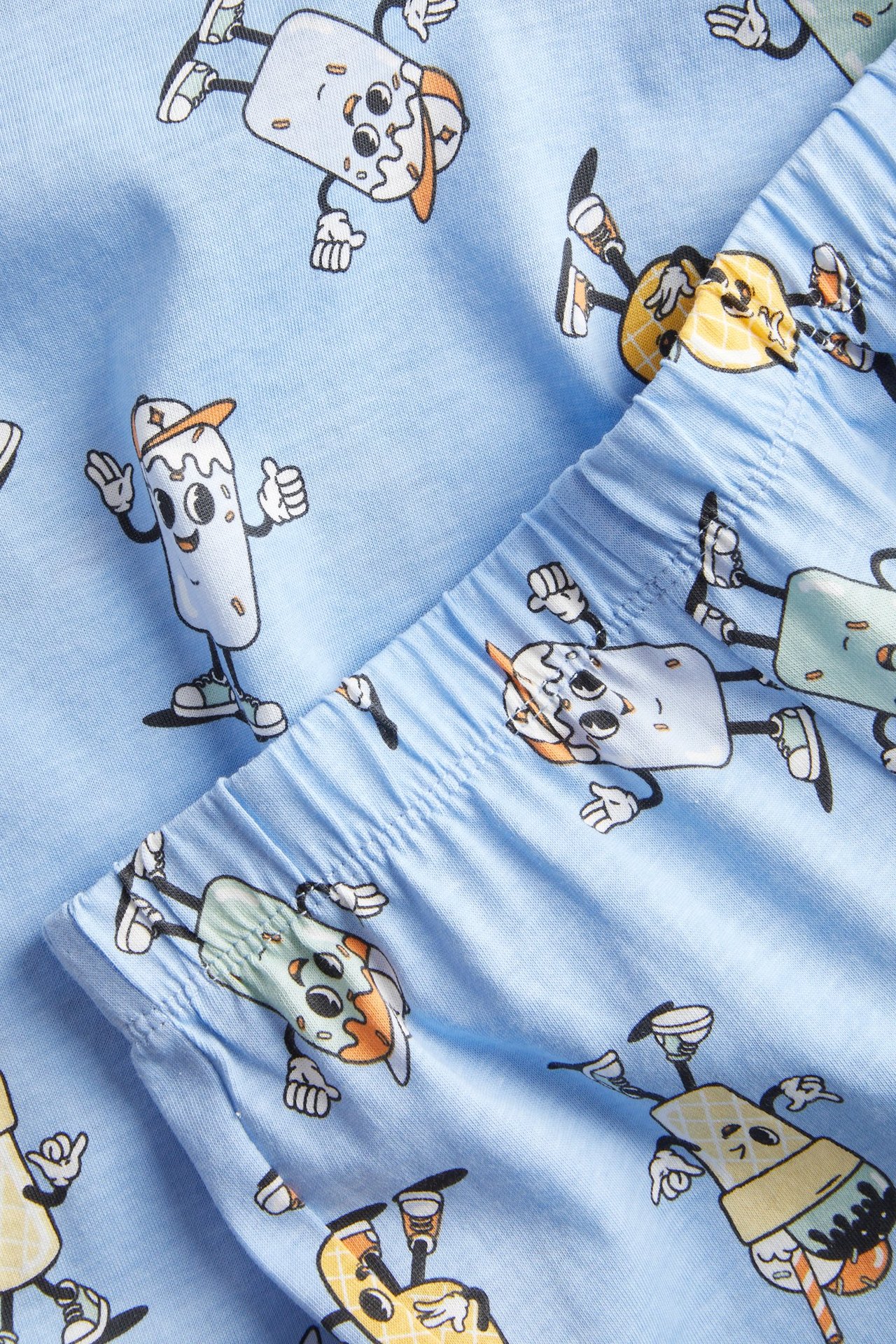 Zbliżenie na jasnoniebieską bawełnianą piżamę dziecięcą, z animowanym wzorem lodów i elastycznym pasem.