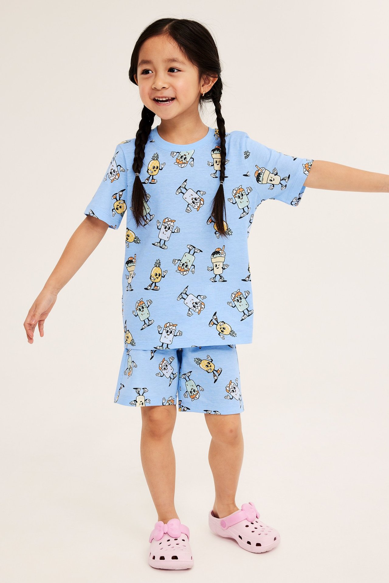 Edestä, lapsi yllään vaaleansininen kuviollinen lyhythihainen puuvillapyjama ja vaaleanpunaiset kengät.