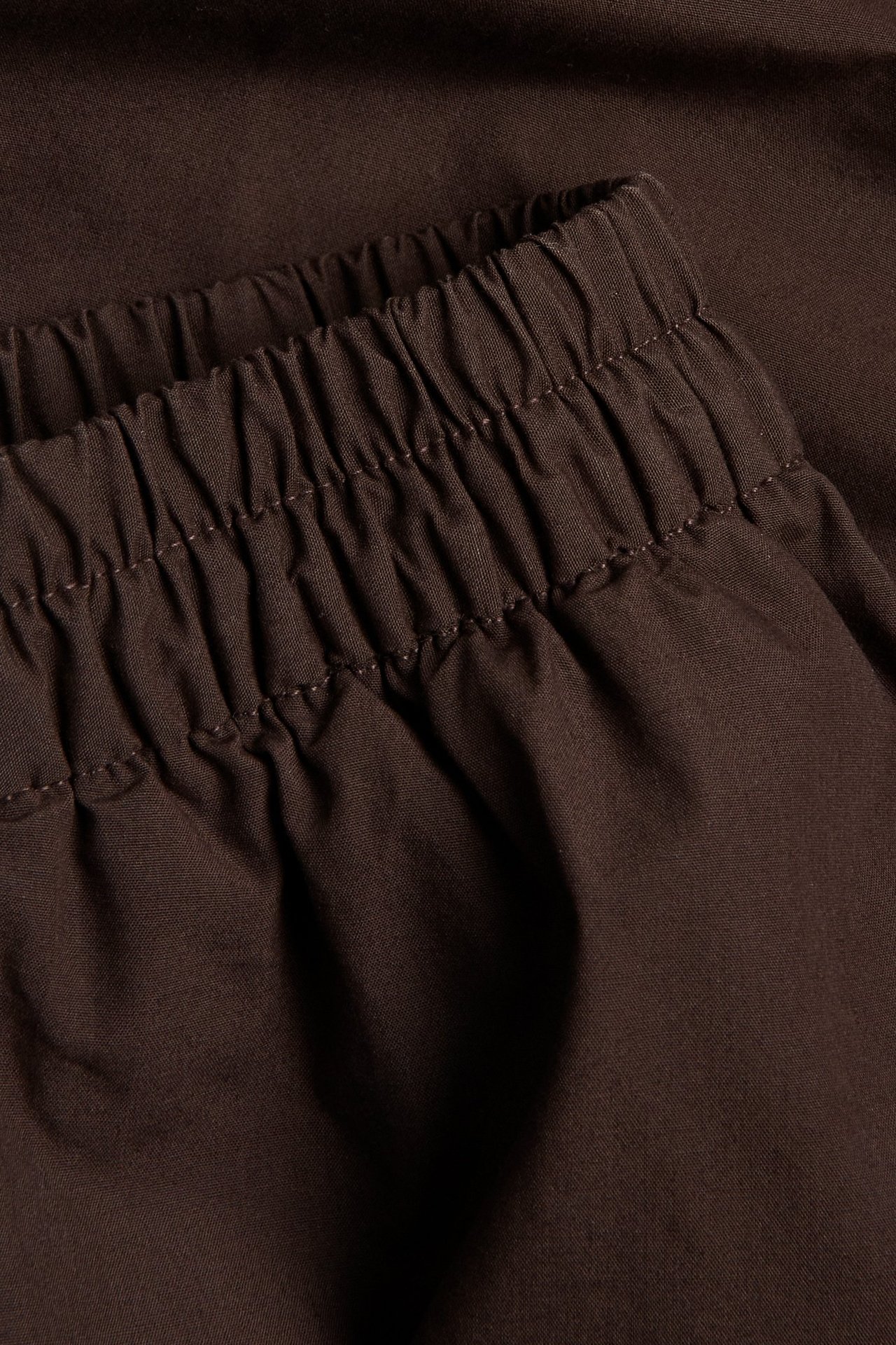 Zbliżenie na ciemnobrązową spódnicę z popeliny bawełnianej z elastyczną talią.