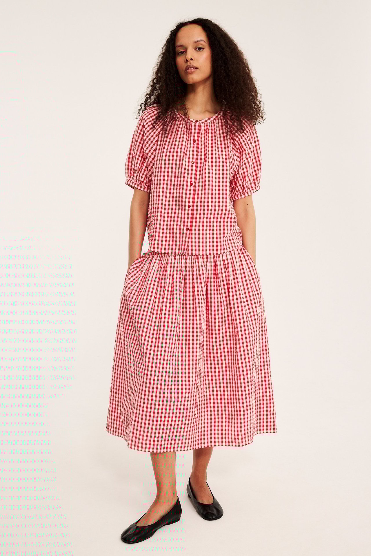 Framifrån, kvinna bär röd rutig bäckebölja midikjol, matchande topp och svarta ballerinaskor.