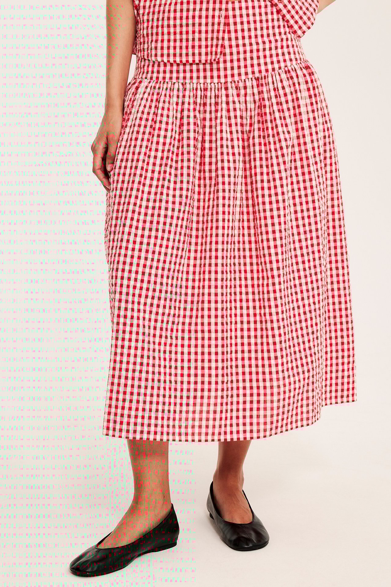 Widok z przodu kobiety w czerwono-białej kraciastej spódnicy midi z krepy, pasującym topie i czarnych butach.