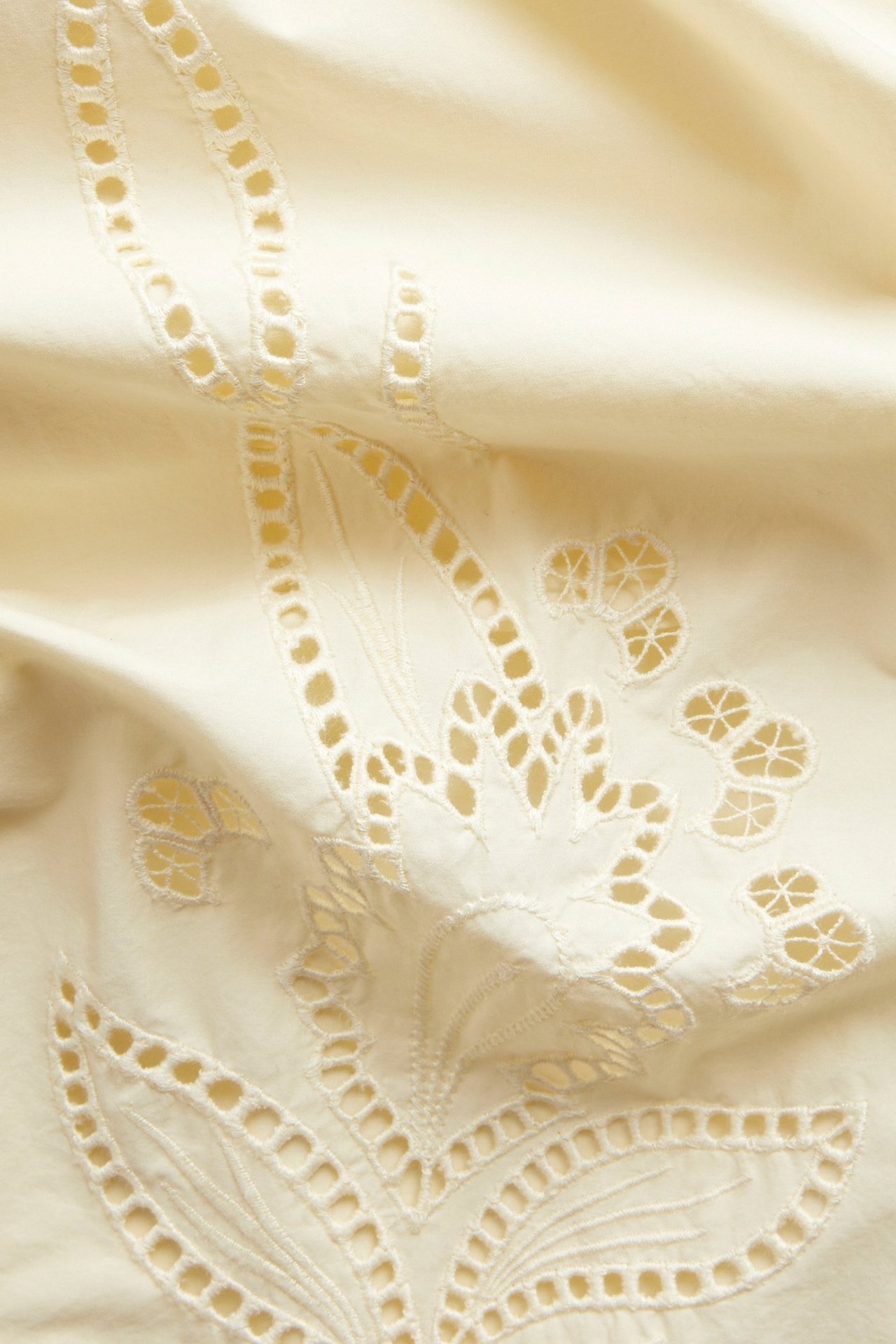 Zbliżenie jasnej żółtej spódnicy z popeliny bawełnianej z białym haftem i wycięciami.