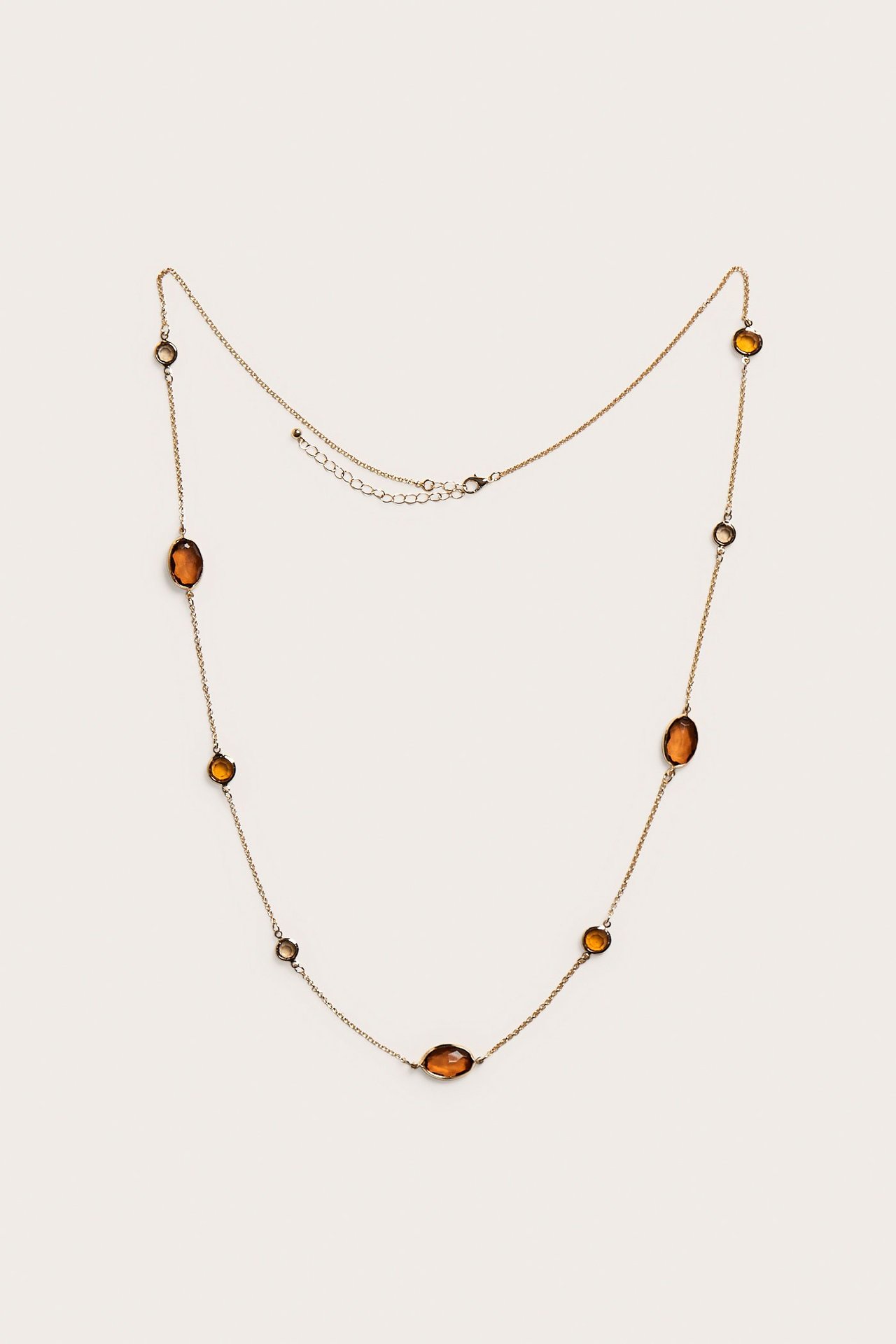 Widok z przodu długiego złotego naszyjnika z równomiernie rozmieszczonymi bursztynowymi kamieniami z tworzywa i zapięciem.