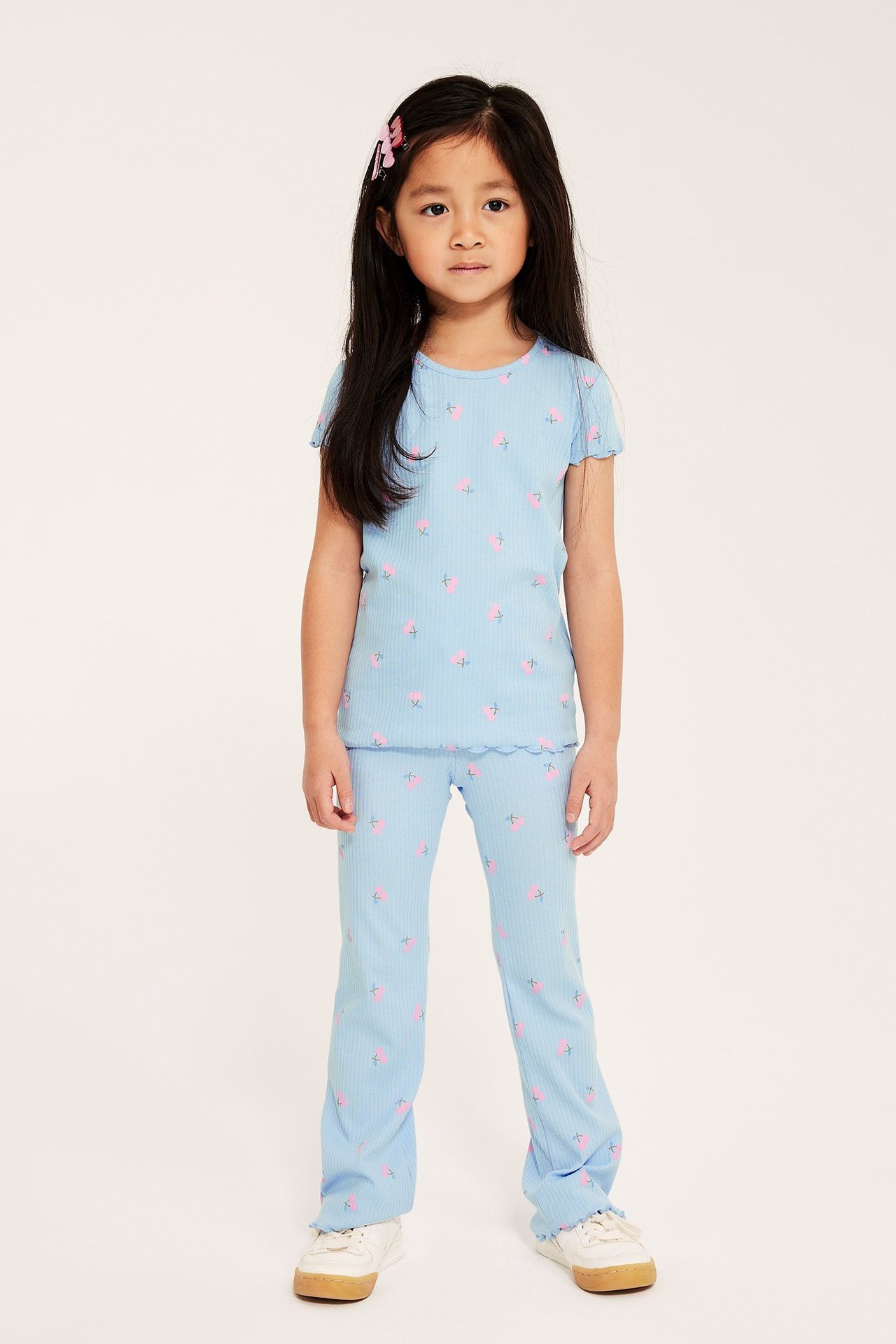 Widok z przodu dziecka w jasnoniebieskich prążkowanych legginsach dzwonach z nadrukiem wiśni i pasującej koszulce.