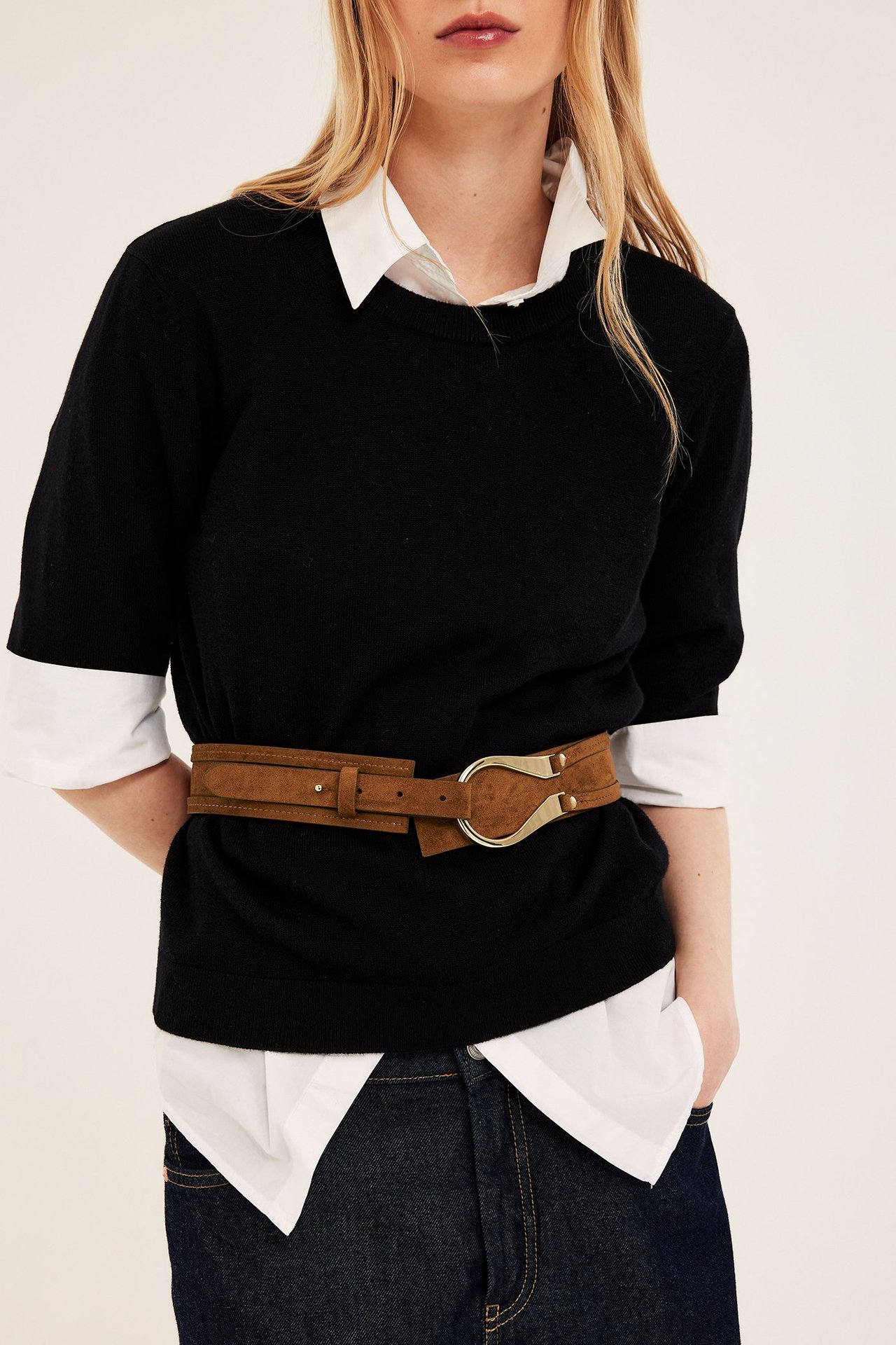 Närbild av kvinna med ljusbrunt mockaimitationsbälte, guldfärgat spänne, över svart tröja och vit skjorta.