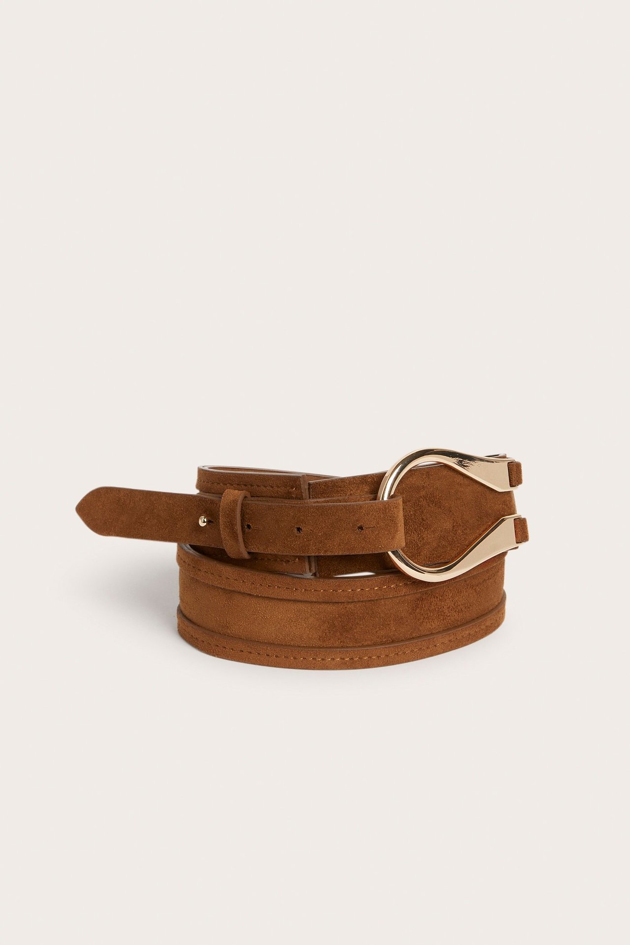 Närbild framifrån på ett ljusbrunt bälte i fuskmocka med ett guldfärgat vikbart spänne.