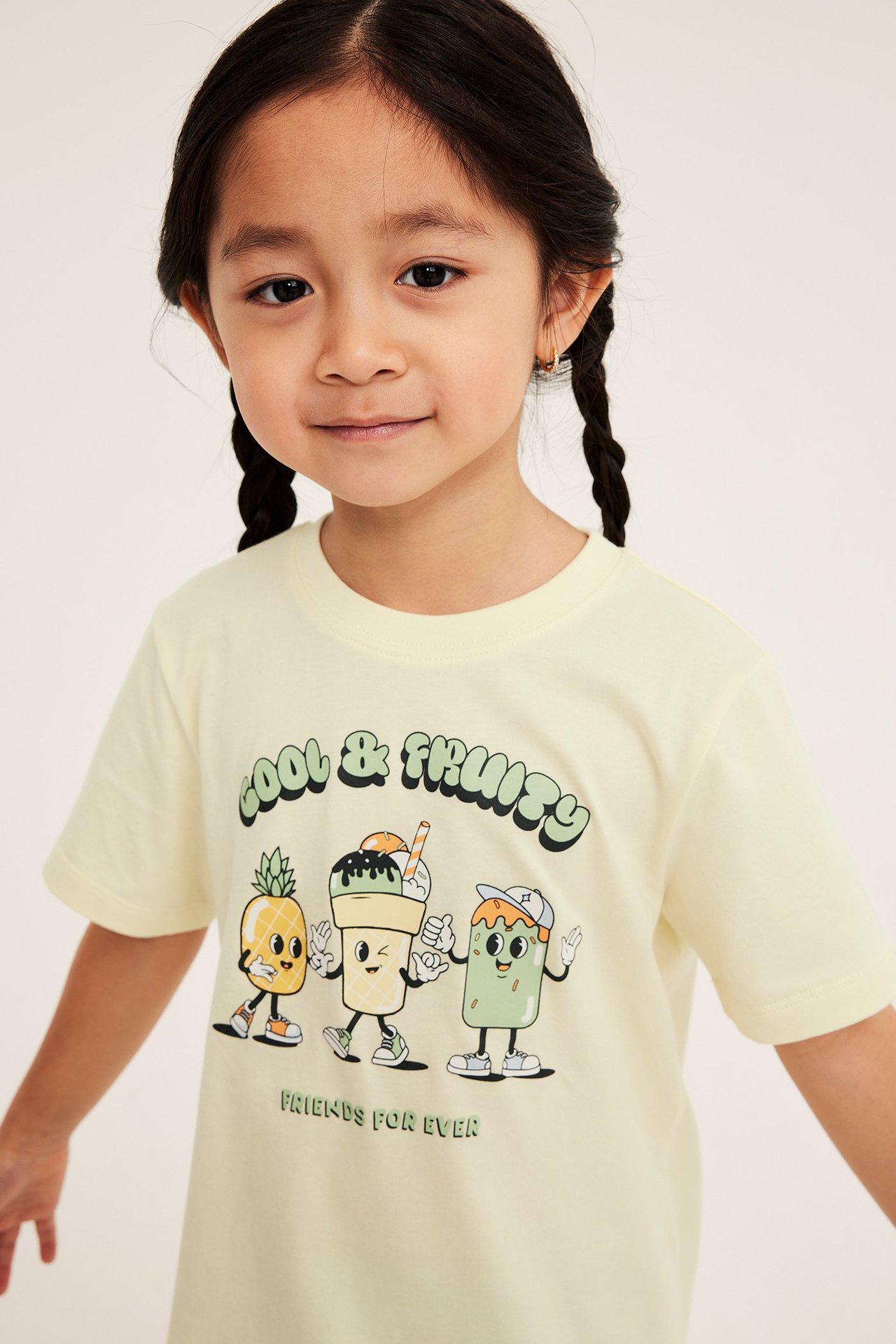Framsida av ett barn som bär en ljusgul kortärmad t-shirt i bomull med "Cool & Fruity"-tryck.