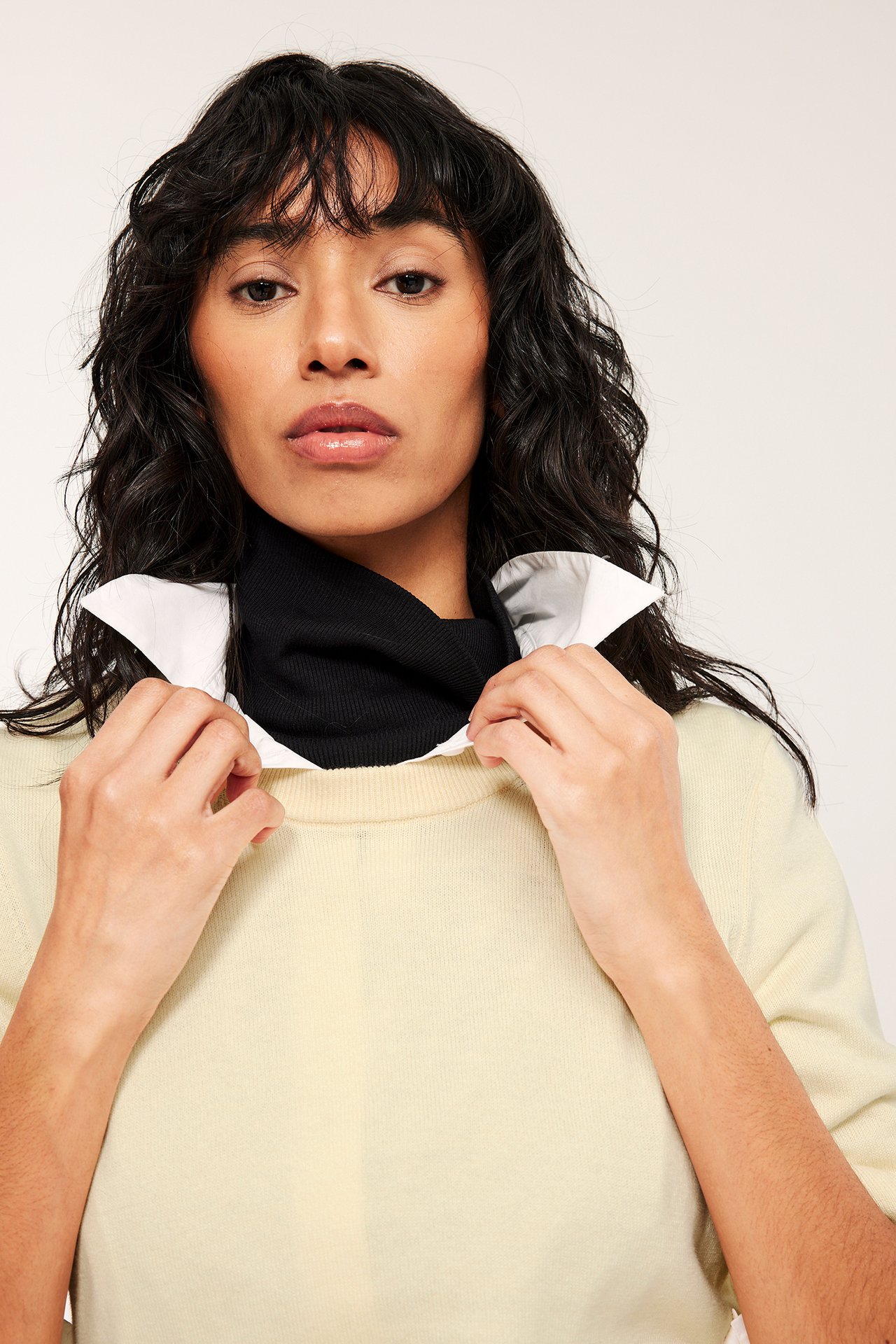 Widok z przodu: kobieta w jasnożółtym cienkim swetrze na czarnym golfie i białym kołnierzyku.