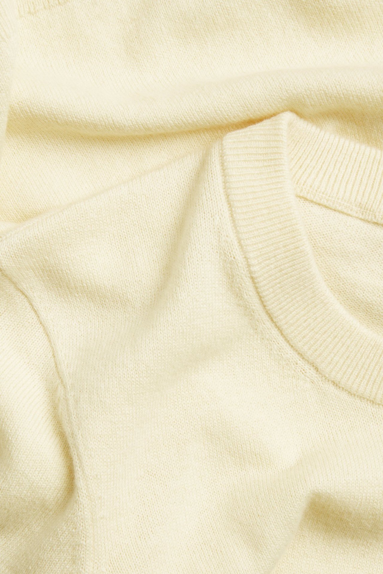 Zbliżenie na jasnożółty, drobno dziany, krótkorękawowy sweter z wełnianej mieszanki z dekoltem w ściągacz.