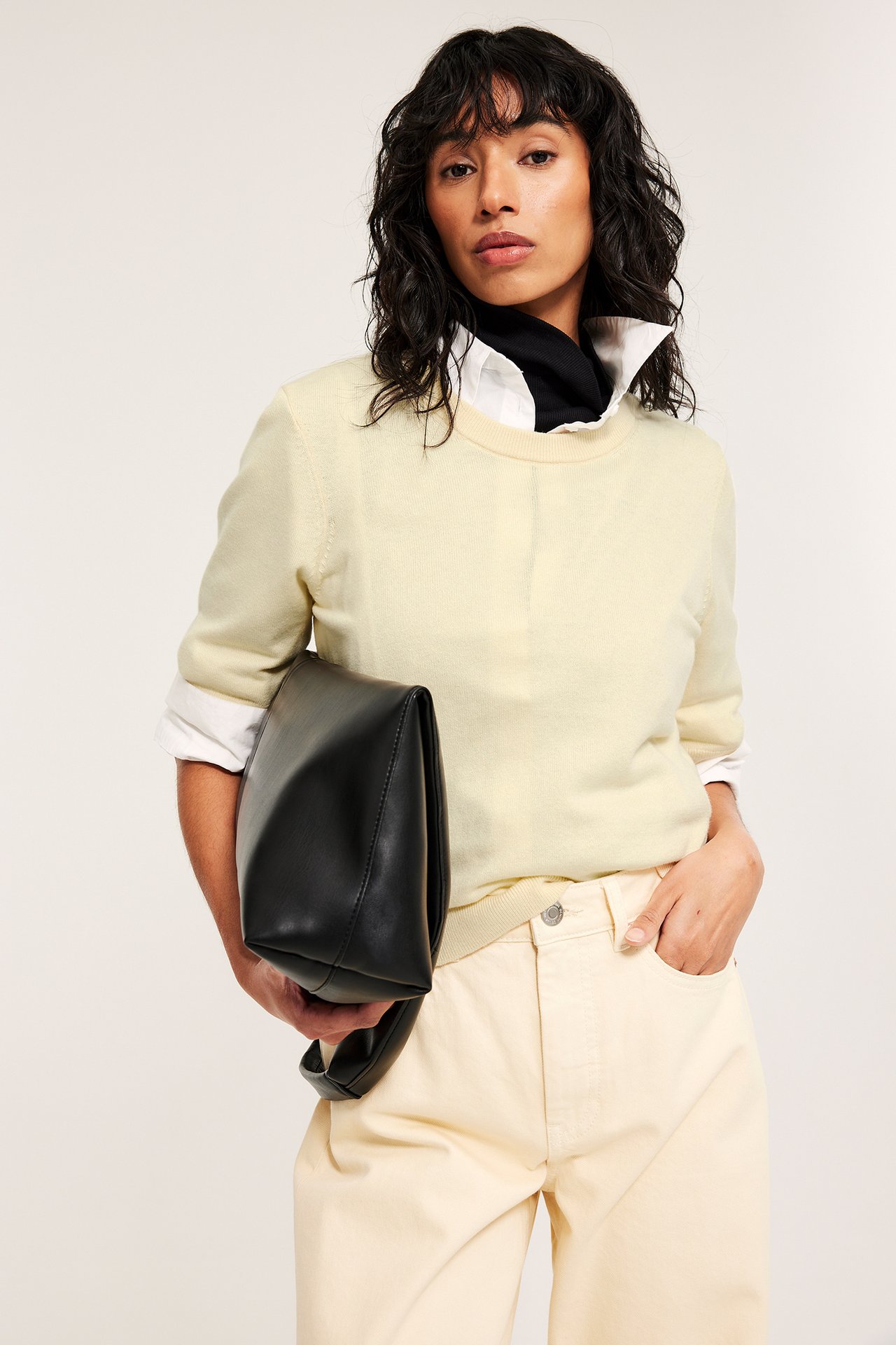 Widok z przodu: Kobieta w jasnożółtym swetrze z mieszanki wełny na białej koszuli, jasnożółte spodnie, trzyma czarną torbę skórzaną.