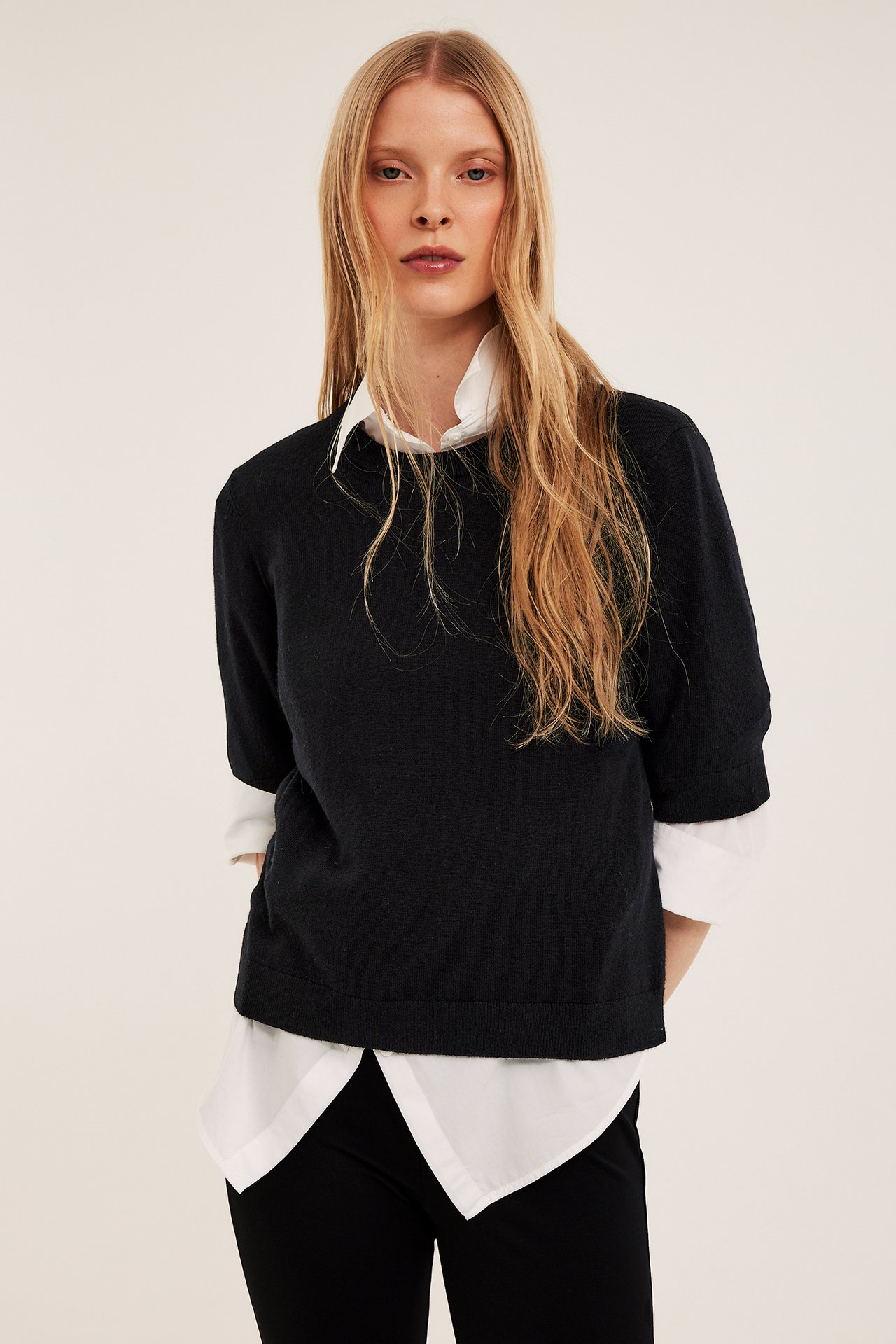 Widok z przodu: Kobieta w czarnym krótkim swetrze na białej koszuli i czarnych spodniach.
