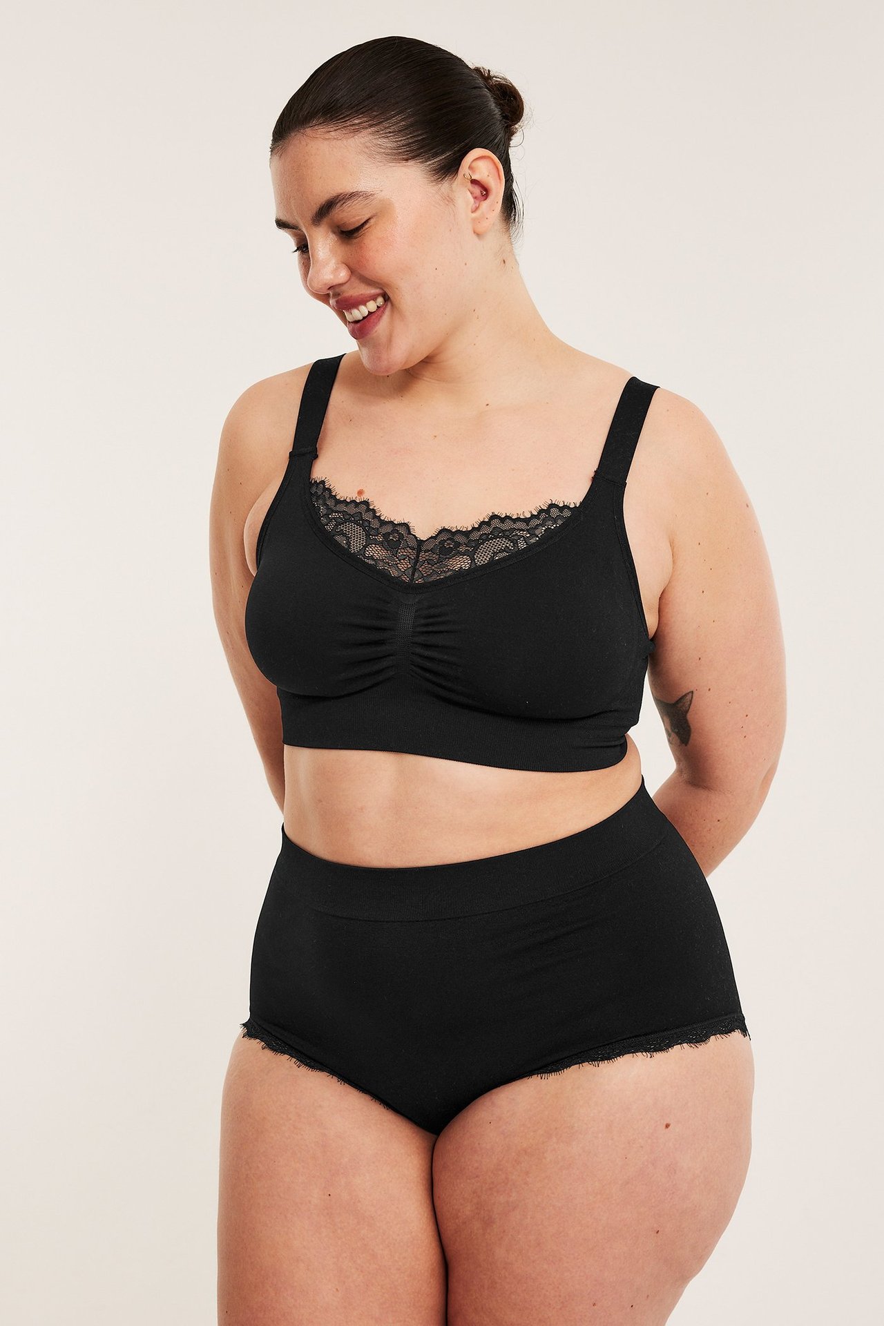 Widok z przodu uśmiechniętej kobiety w czarnym, bezszwowym biustonoszu bez fiszbin z koronką i pasującymi figami.