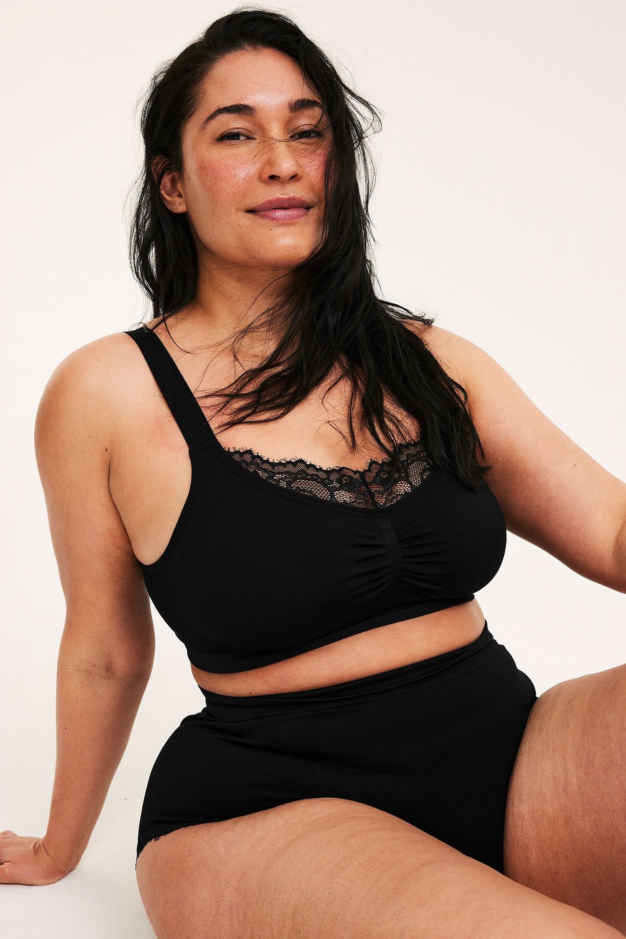 Framifrån: kvinna i svart sömlös bygellös bh med spetsdetalj och matchande hög midjetrosa.