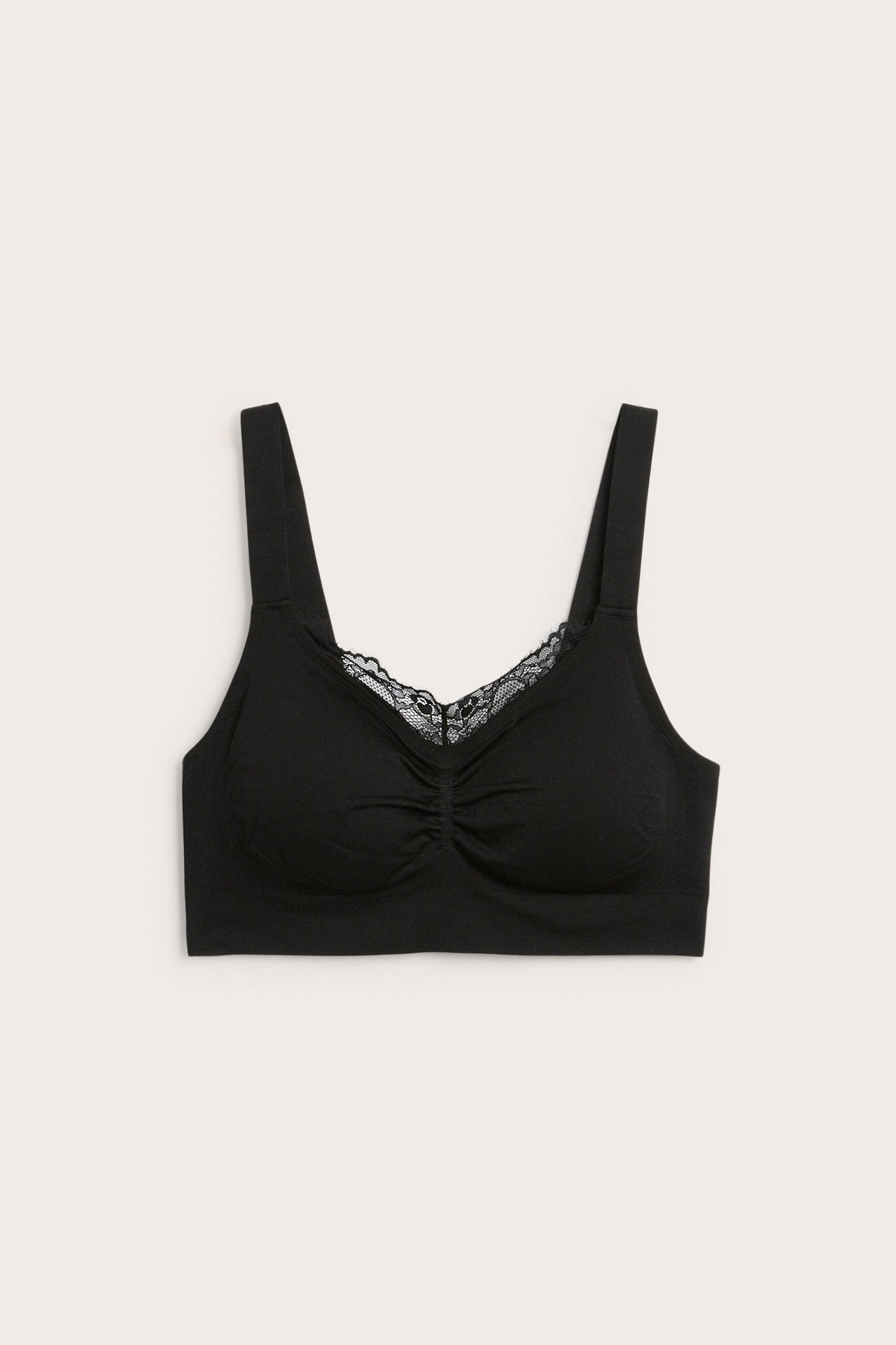 Widok z przodu czarnego bezszwowego biustonosza bez fiszbin, z szerokimi ramiączkami, marszczeniem i koronką przy dekolcie.