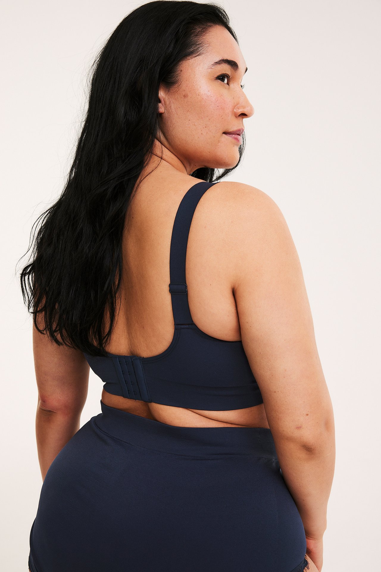 Ryggvy av kvinna i mörkblå sömlös bygellös bh med hyskknäppning och matchande sömlösa trosor.
