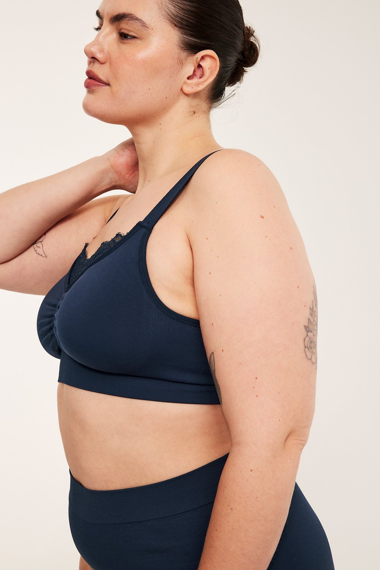 Sidovy av kvinna i mörkblå sömlös bygellös BH med spetskant och breda justerbara axelband.