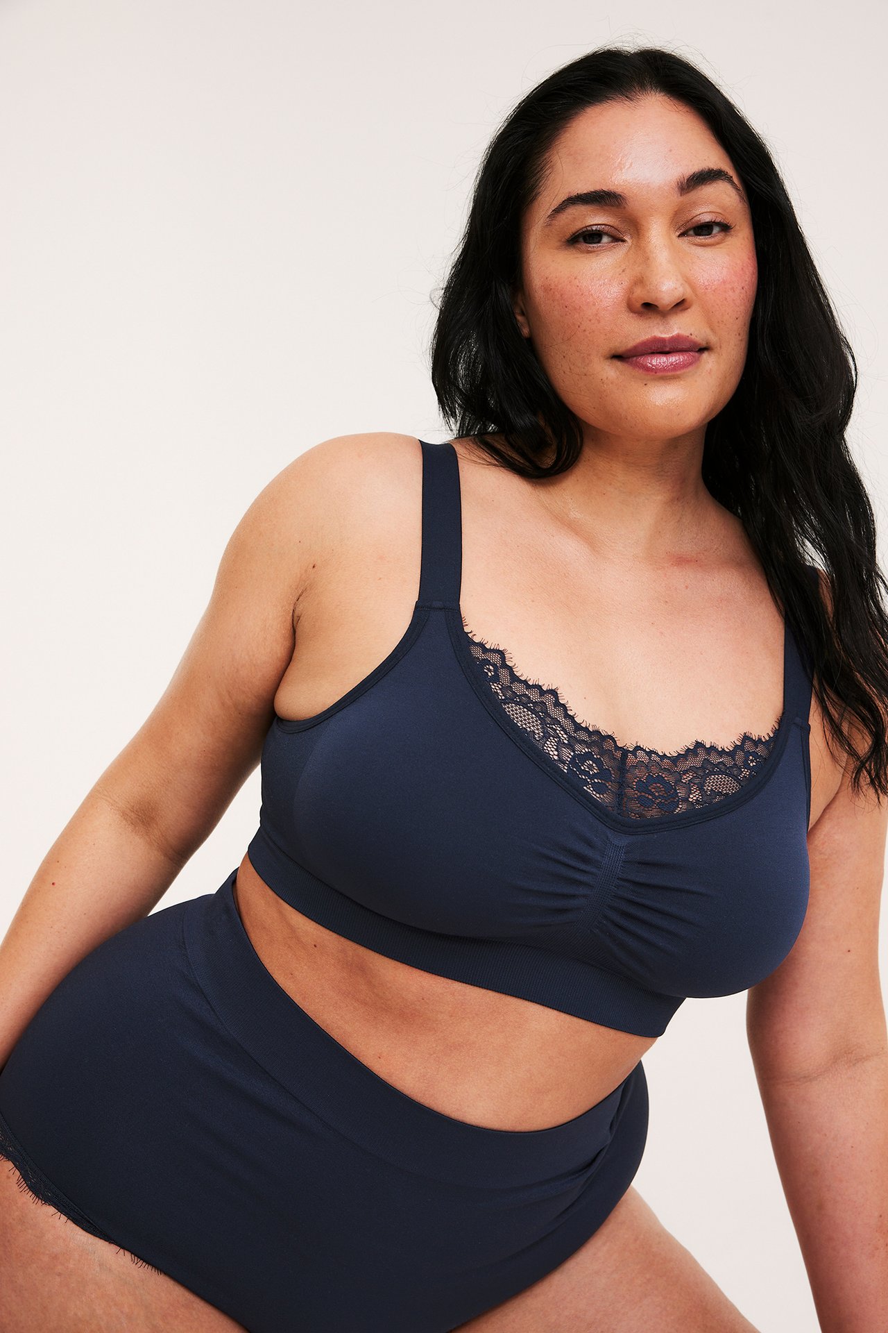 Frontbild av en kvinna i mörkblå sömlös bygellös BH med spetsdetaljer och matchande högmidjade trosor.