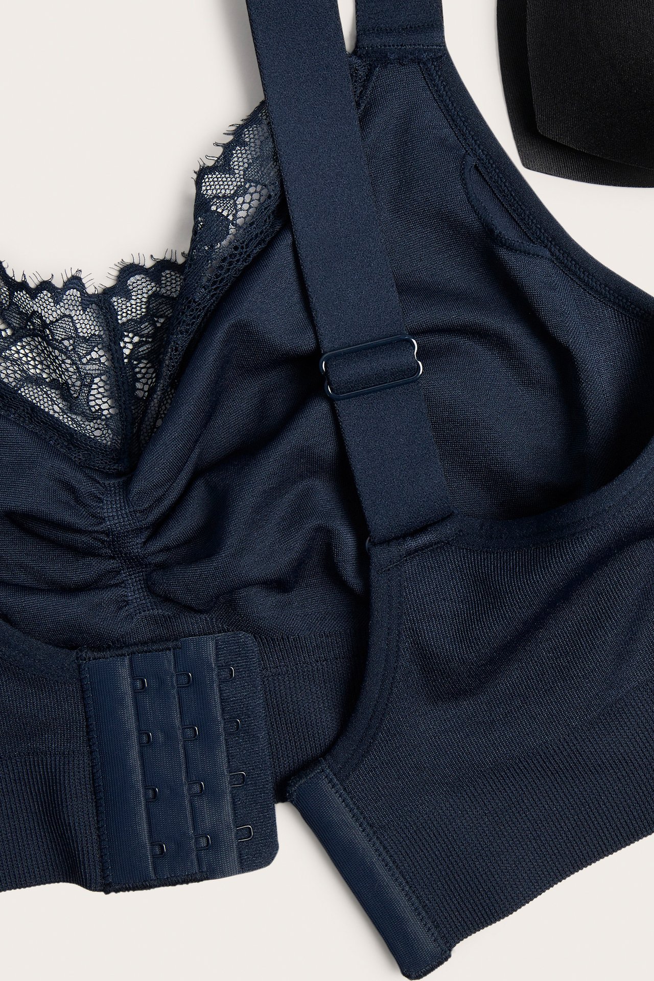 Närbild på en mörkblå bygellös sömlös bh med spetsdetaljer, rynkning, justerbara band och hak- och hyskknäppning.