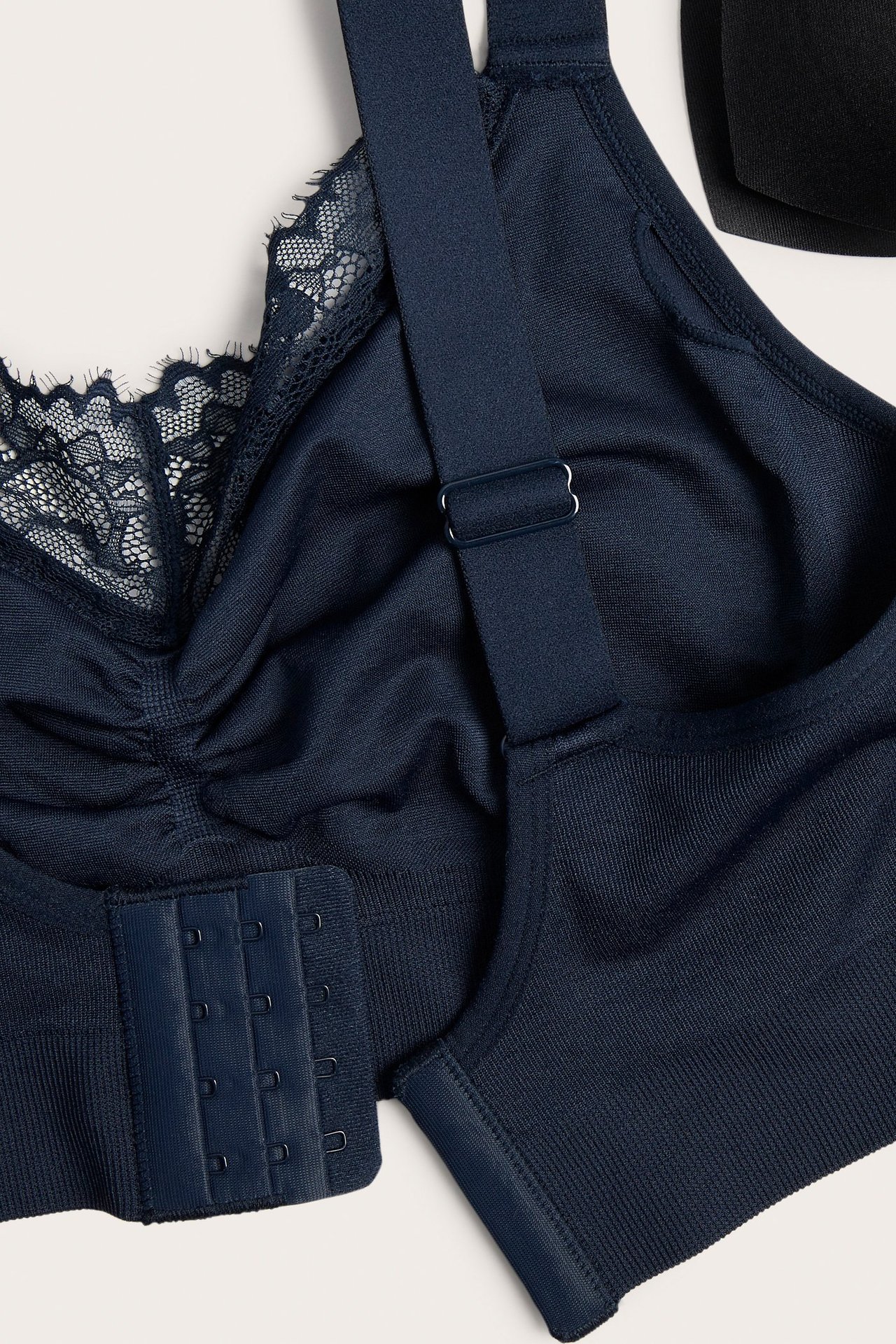 Zbliżenie granatowego, bezszwowego biustonosza bez fiszbin z koronką, marszczeniem, regulowanymi ramiączkami i haftkami.