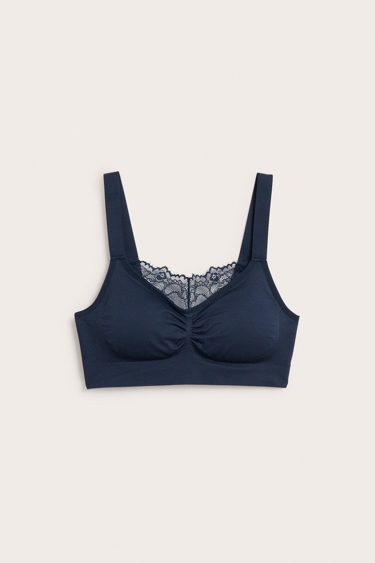 Framifrån, mörkblå sömlös bygellös bh med breda axelband, rynkad front och vacker spetskant.