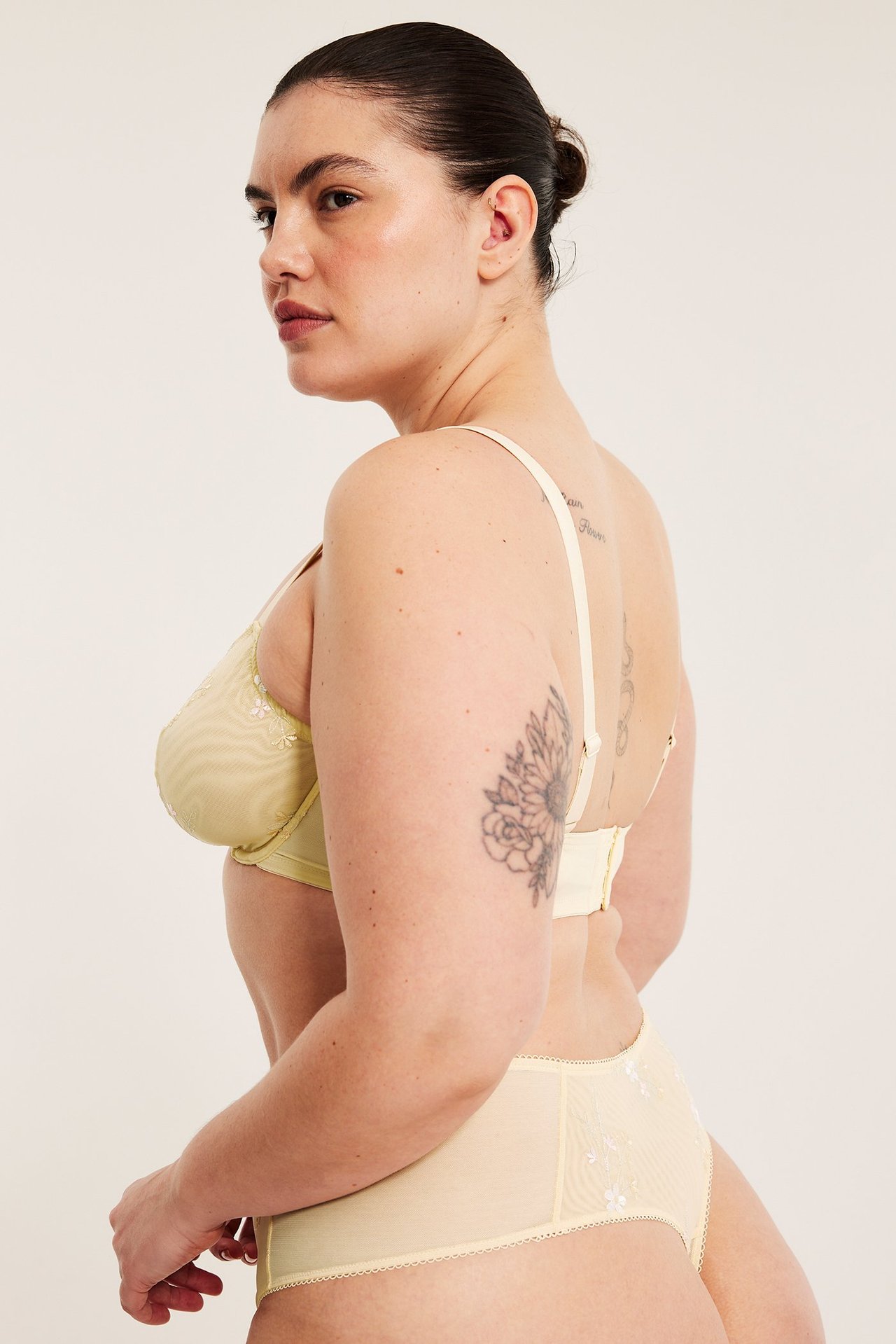 Sidebilde av kvinne i lys gul spile-BH i mesh med broderte blomster og matchende truse.