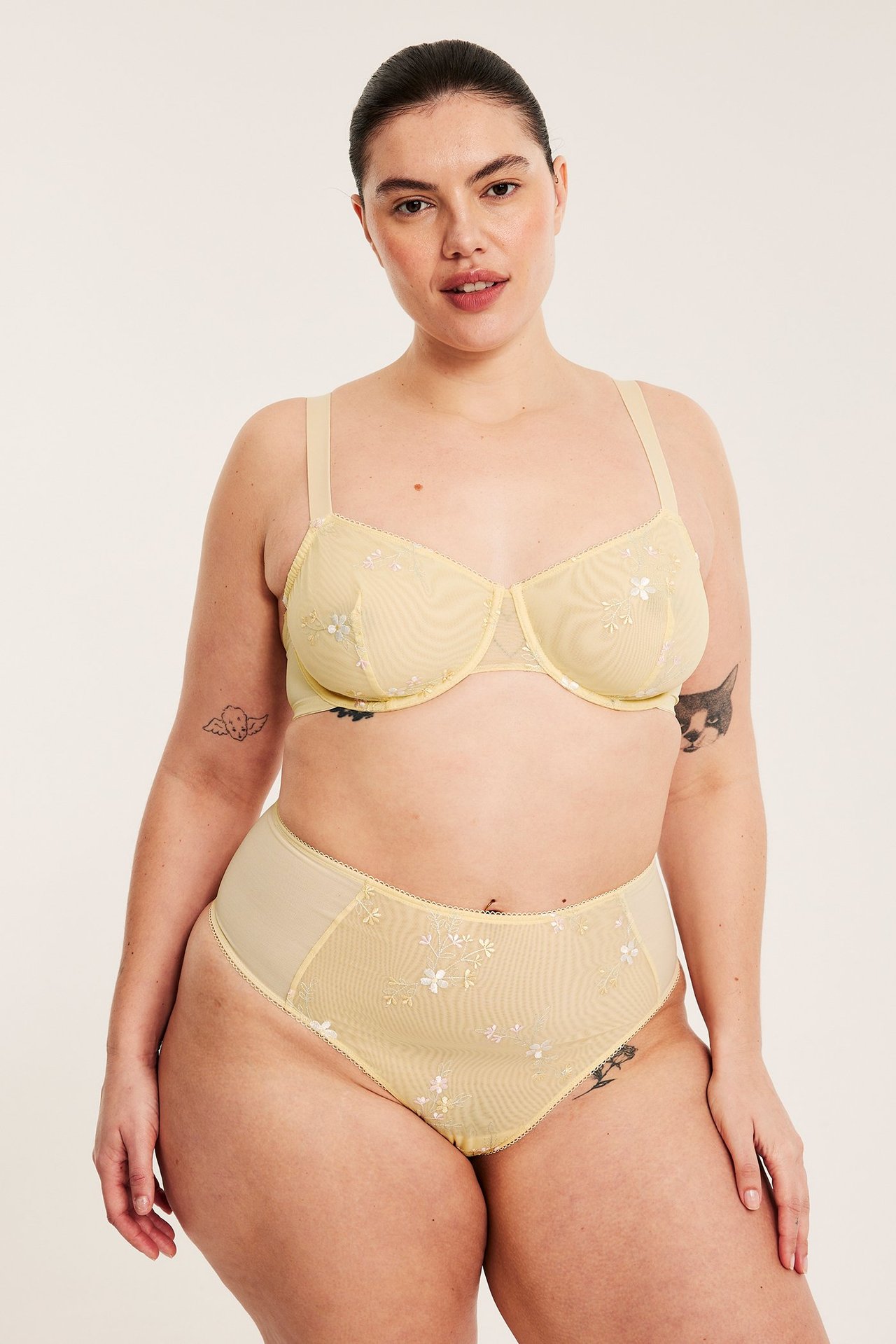 Nainen edestäpäin yllään vaaleankeltainen mesh-kaarinliivit ja yhteensopivat korkeavyötäröiset pikkuhousut kukkakirjailulla.