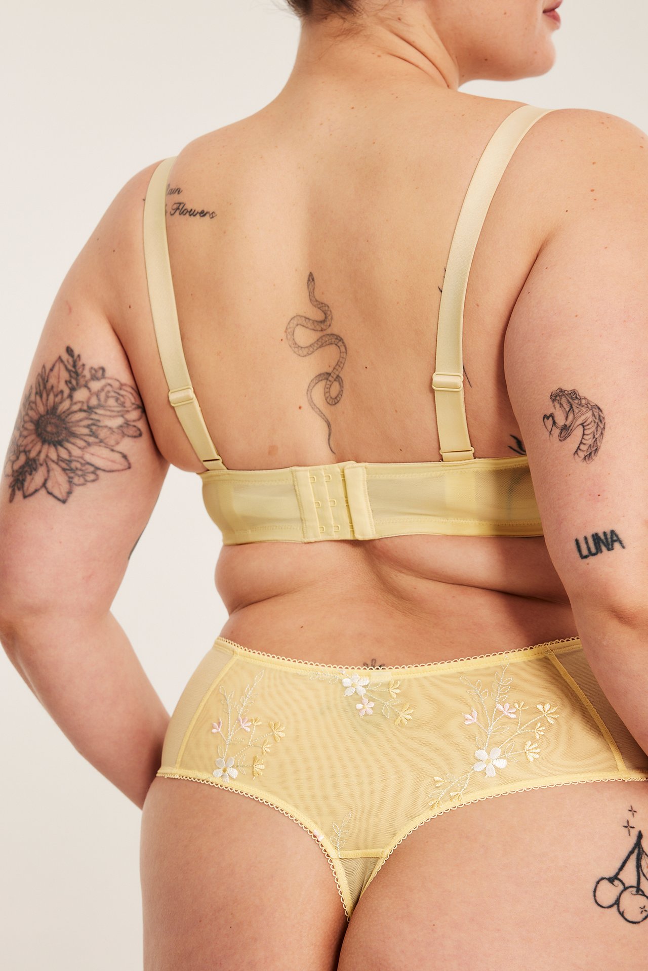 Naisen selkä, vaaleankeltainen kirjailtu korkeavyötäröinen stringi ja rintaliivit.